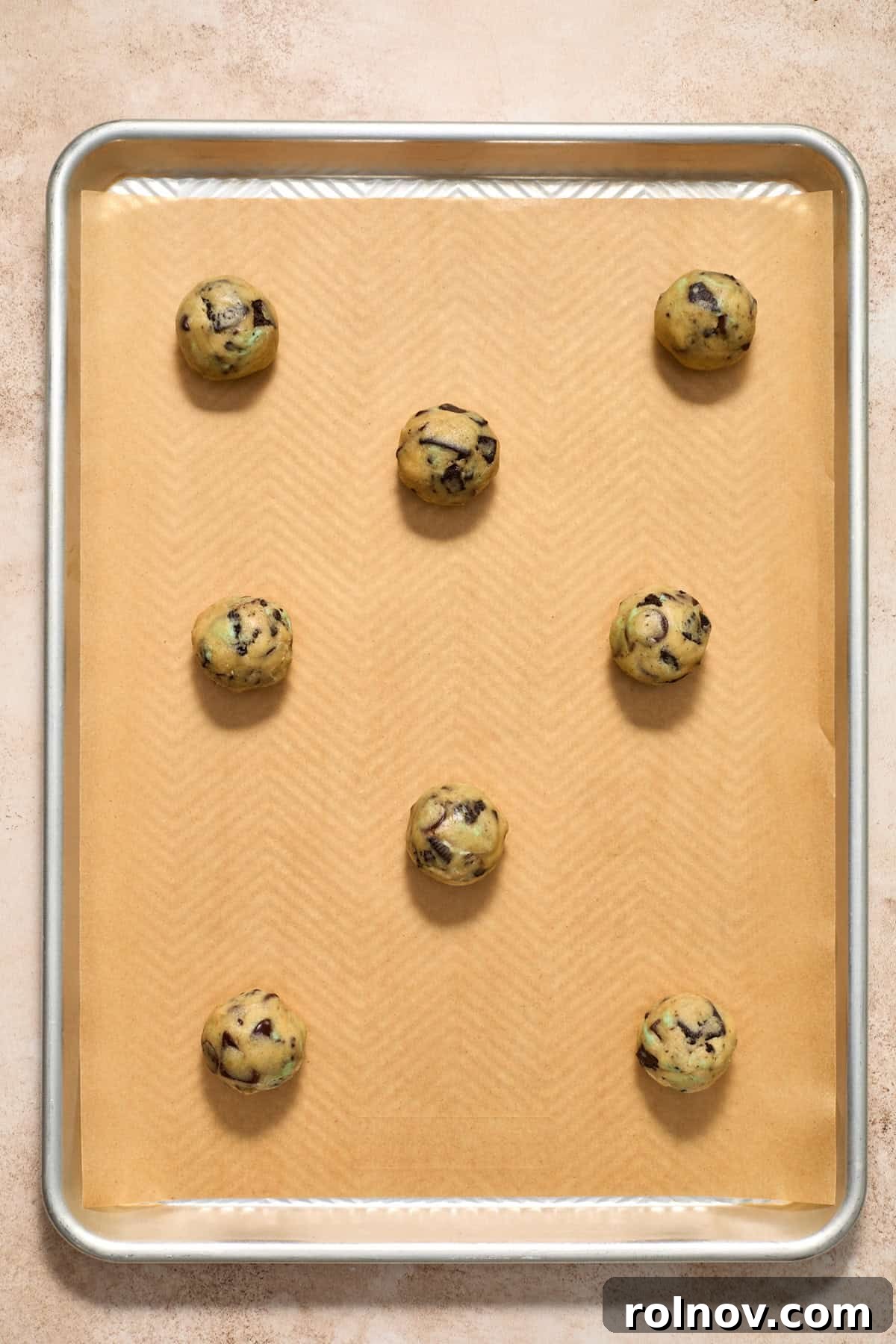 Scooped cookie dough balls evenly arranged on a parchment-lined cookie pan, ready for baking.