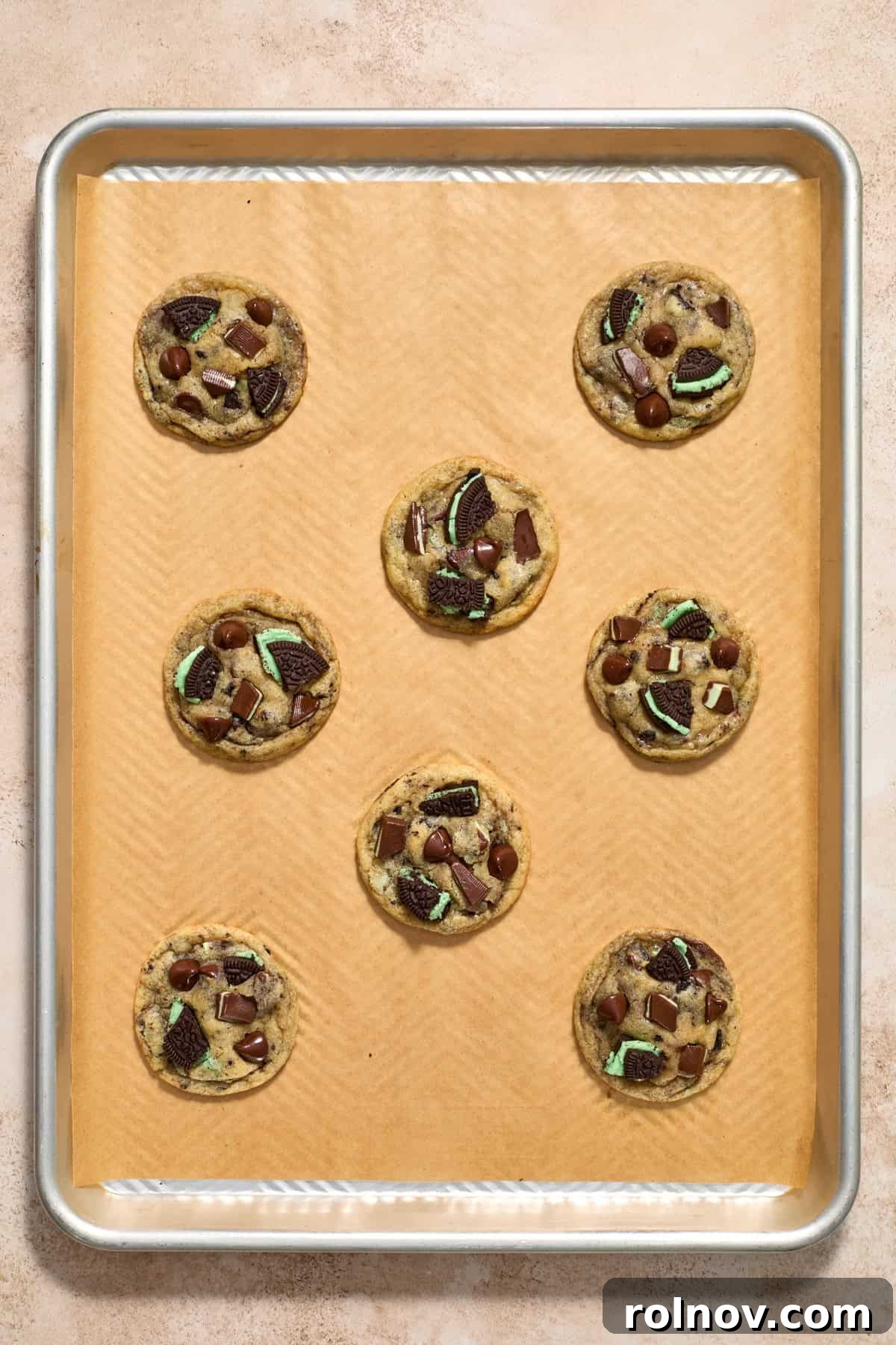 Freshly baked mint chocolate chip cookies cooling on a parchment-lined baking pan, showcasing their golden edges.