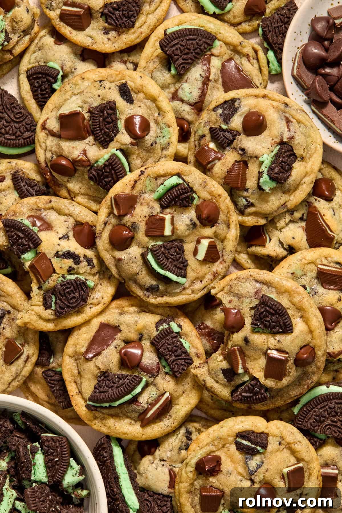 Arrangement of freshly baked mint chip cookies on a surface, with additional mint Oreos and chocolate chips scattered nearby.