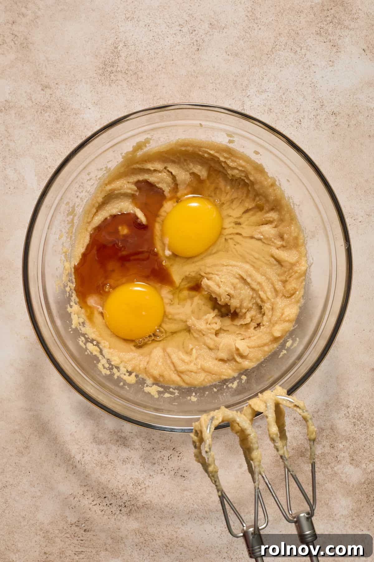 Combined butter and sugars in a bowl with two large eggs and vanilla extract freshly added, ready for the next mixing stage.