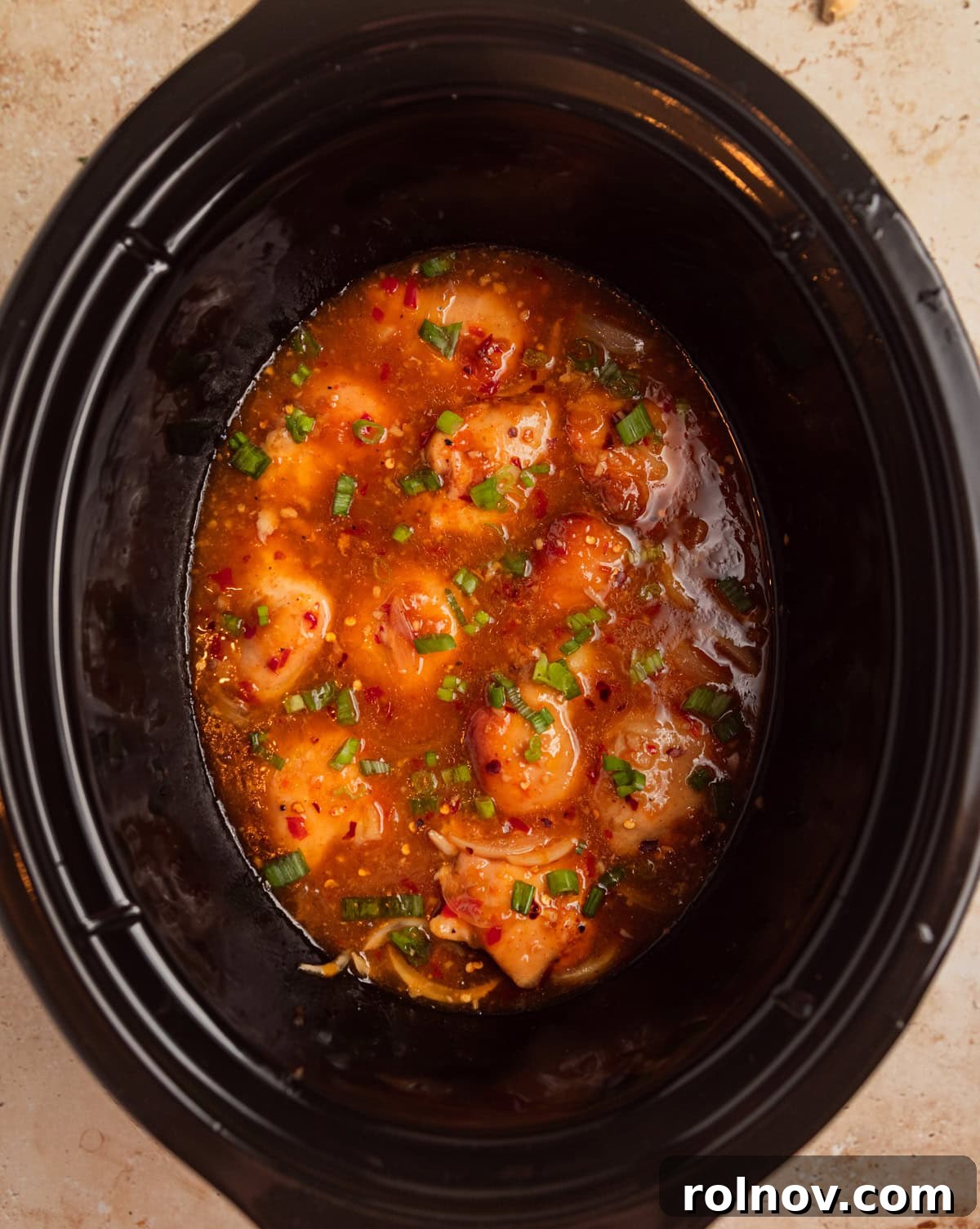 Sweet and Savory Apricot Slow-Cooked Chicken 9 Slow cooker apricot chicken in pot topped with sliced green onions on top.