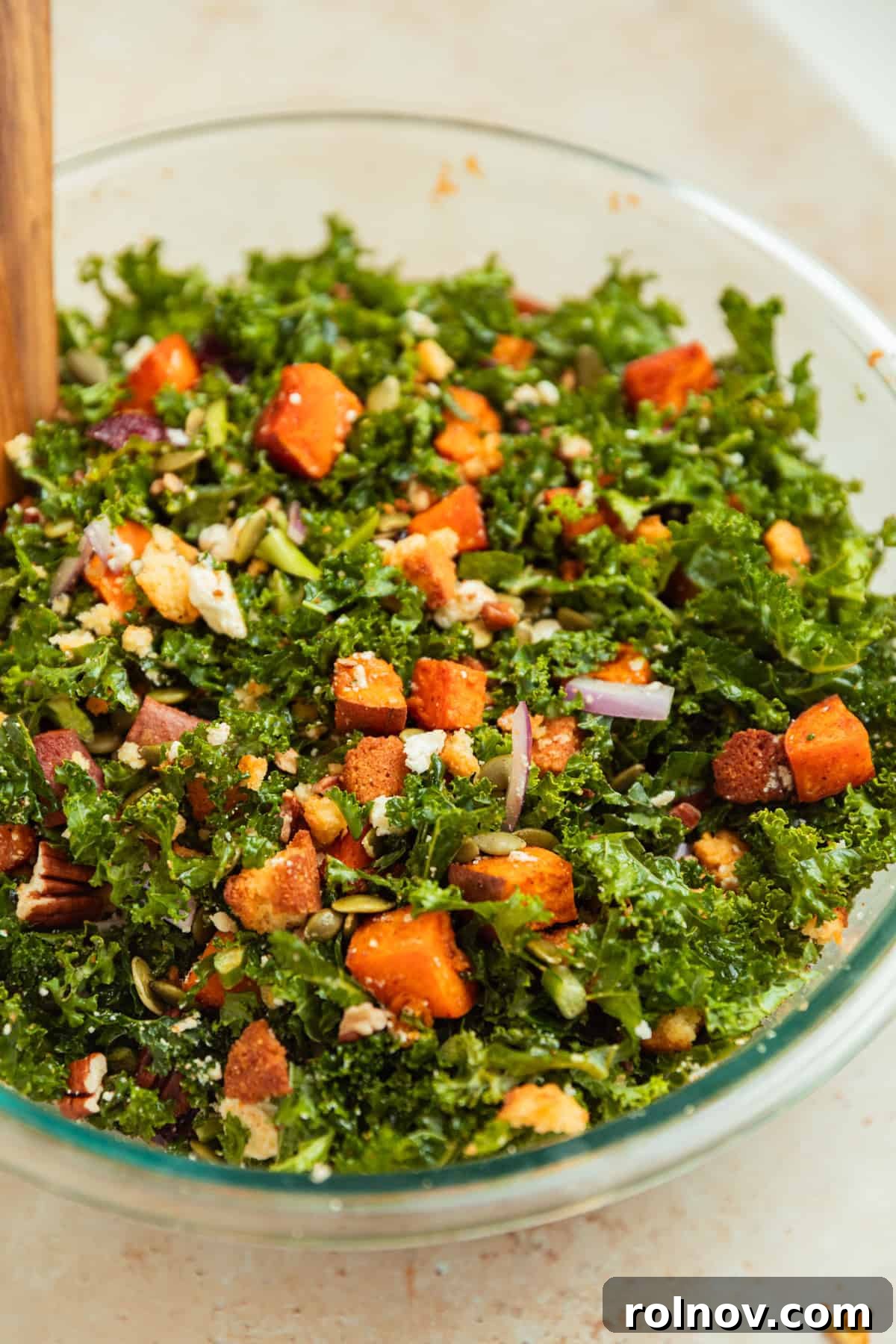 Roasted Sweet Potato Kale Salad 11 A beautifully tossed sweet potato kale salad in a large glass bowl, with tongs ready for serving, showcasing its vibrant ingredients.