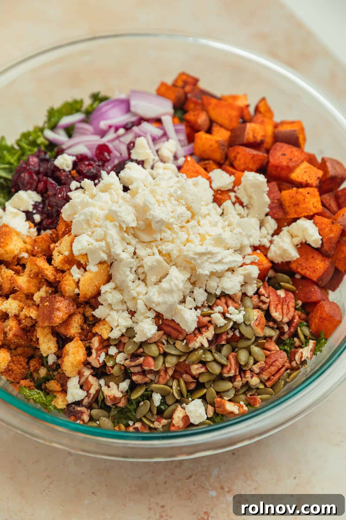 Roasted Sweet Potato Kale Salad 10 A vibrant kale salad in a large bowl, featuring colorful elements like cornbread croutons, dried cranberries, roasted sweet potatoes, and crumbled feta cheese.