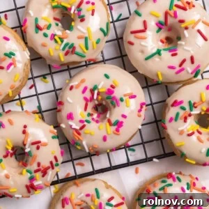 Vanilla baked donuts with maple glaze and rainbow sprinkles on cooling rack.