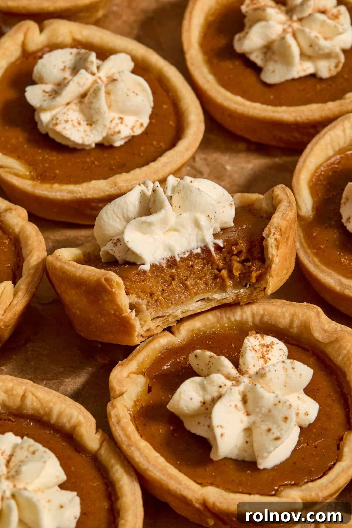 Bite-Sized Pumpkin Delights 13 Miniature pumpkin pies on parchment paper, one with a small bite taken out, revealing the creamy filling and crisp crust.