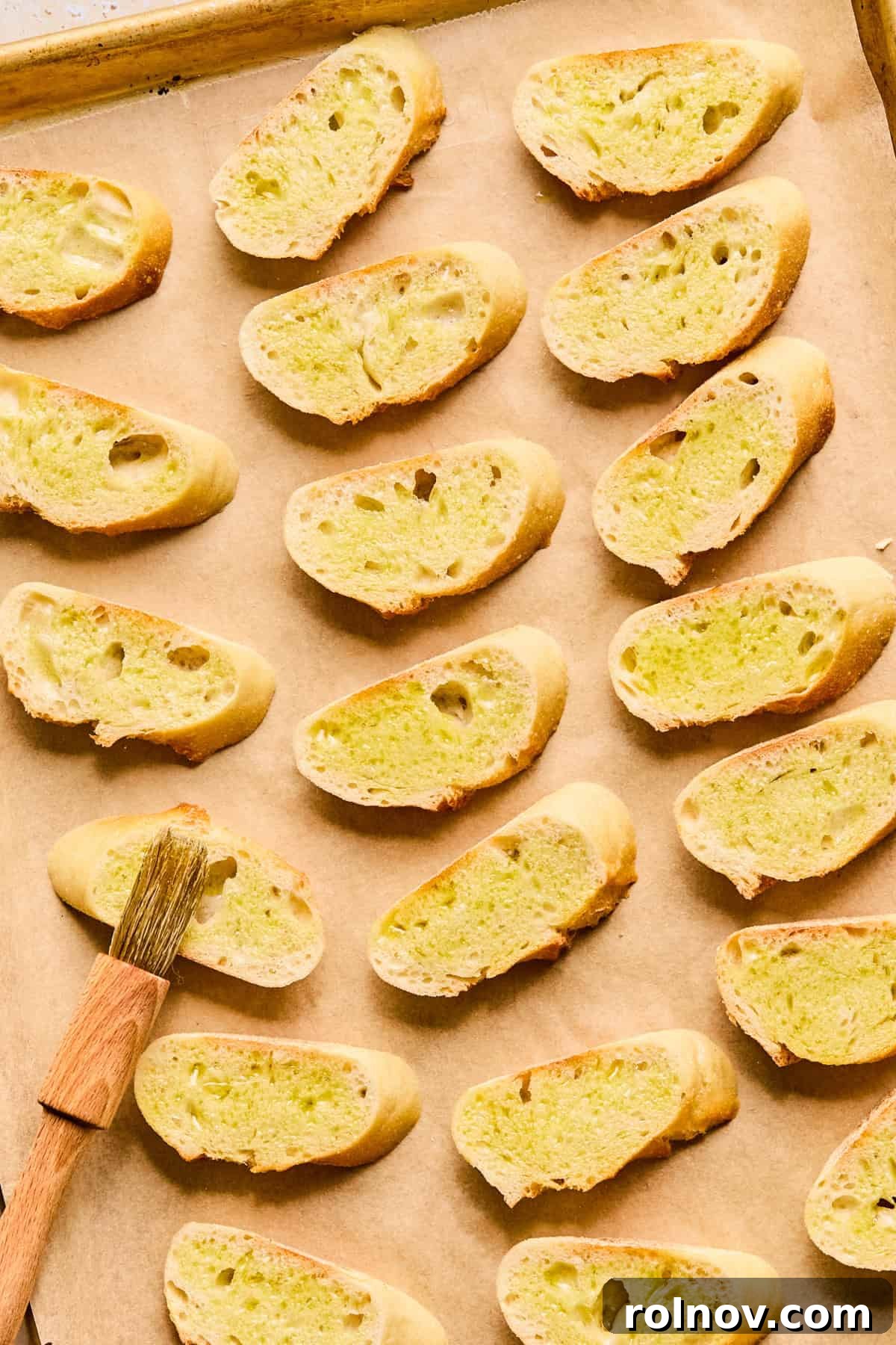 Fresh baguette slices arranged on parchment paper, lightly brushed with olive oil, ready for toasting.