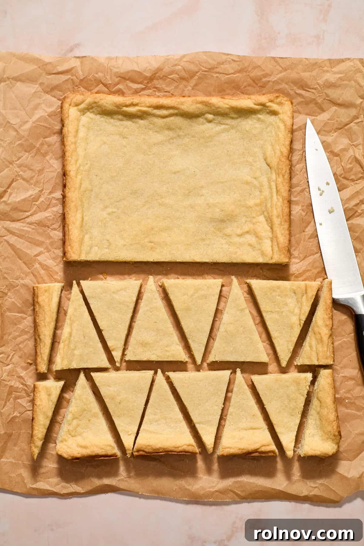 Sugar cookie bars on parchment paper, sliced into festive triangle shapes for Christmas trees.