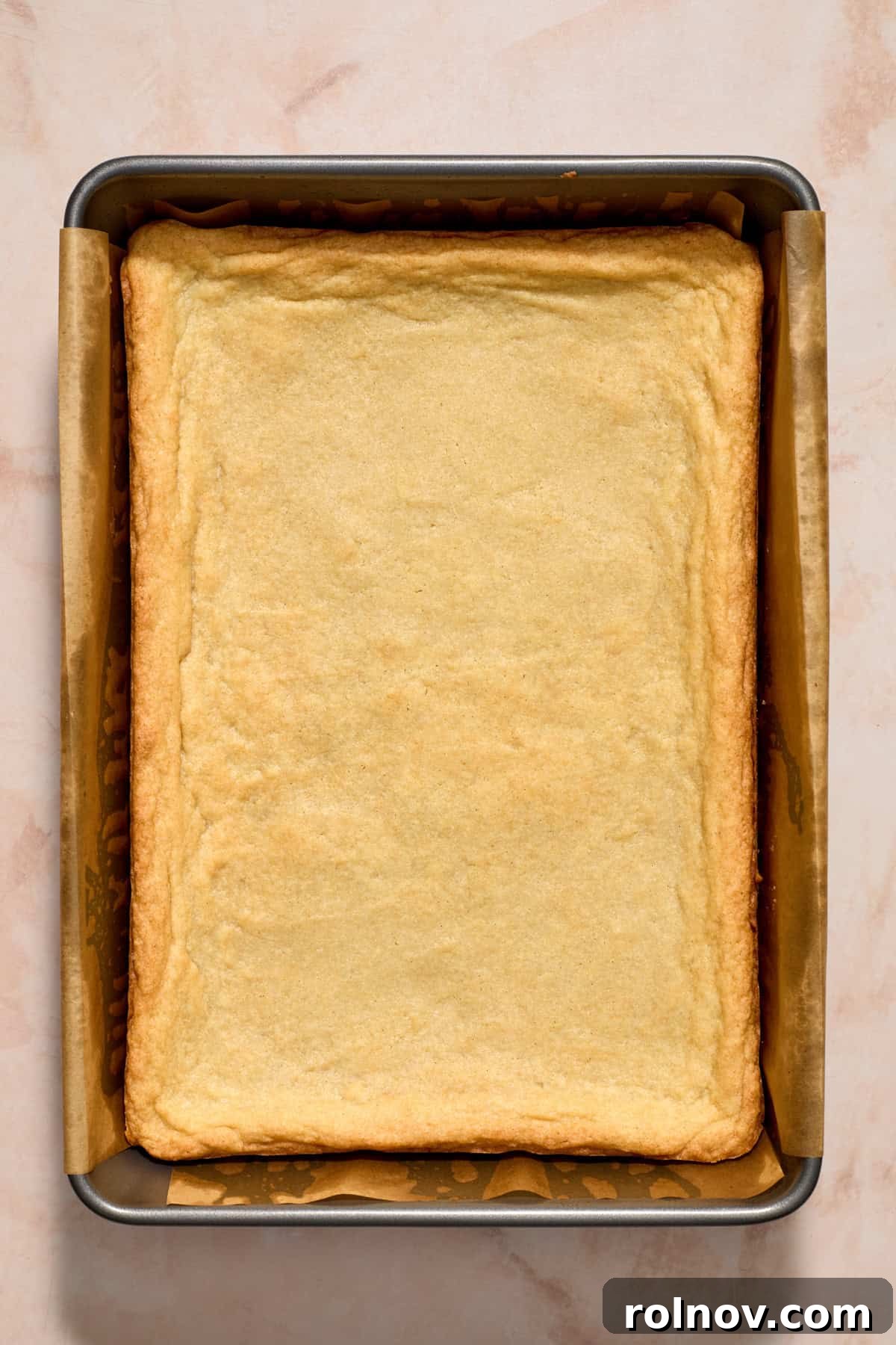 Cooked sugar cookie bar in a baking pan, showing a slightly golden edge.
