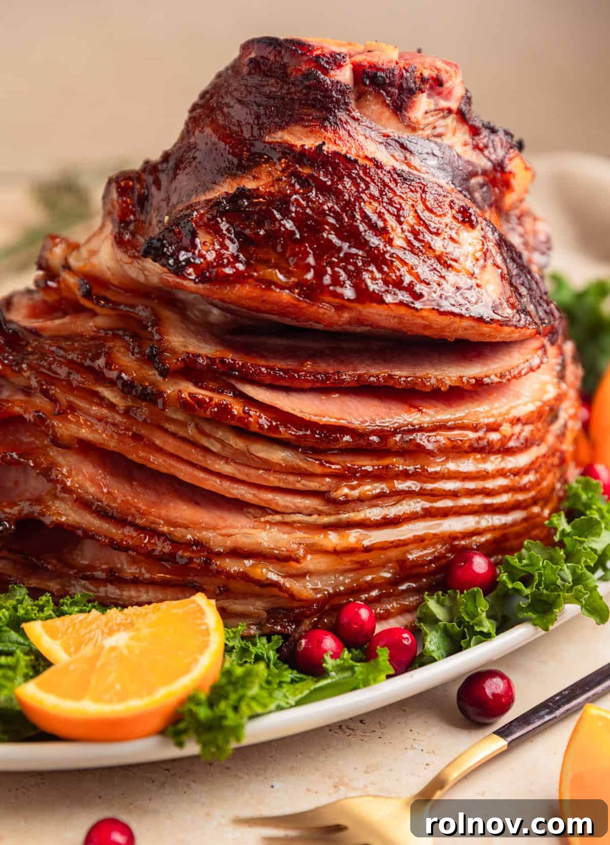 Apricot glazed spiral ham on plate with kale, orange slices and cranberries.