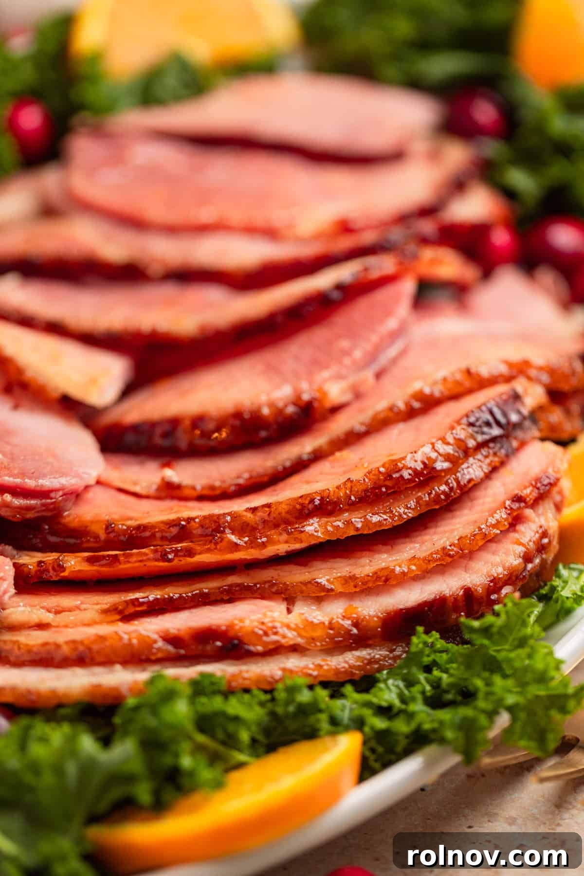 Sliced apricot glazed ham on plate with greens.