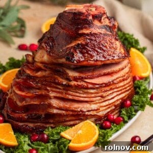 Apricot glazed ham on serving platter with orange slices and cranberries.