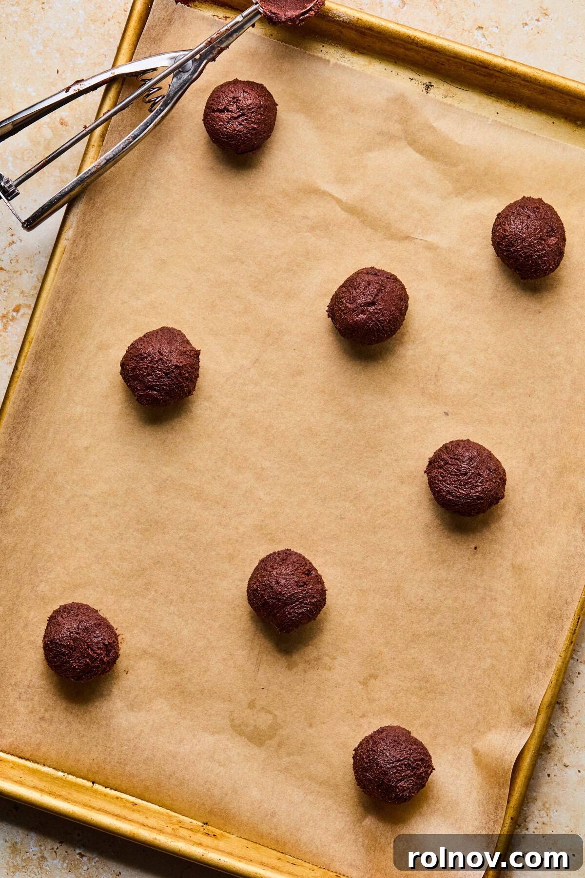 Supernova Brownie Cookies 10 Parchment-lined cookie sheet with perfectly scooped and rolled chocolate cookie dough balls, spaced evenly apart.