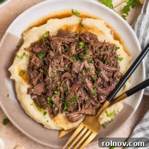 Crock pot shredded beef generously spooned over a bed of creamy mashed potatoes on a plate.