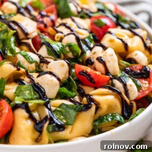 A fresh tortellini caprese salad in a bowl, drizzled with a rich balsamic glaze.