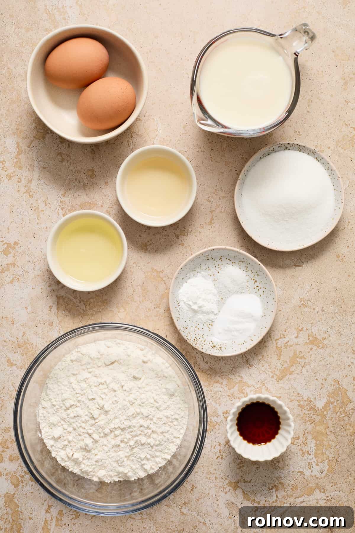 Various dairy-free buttermilk pancake ingredients, including almond milk, vinegar, flour, eggs, and oil, neatly arranged on a kitchen surface.