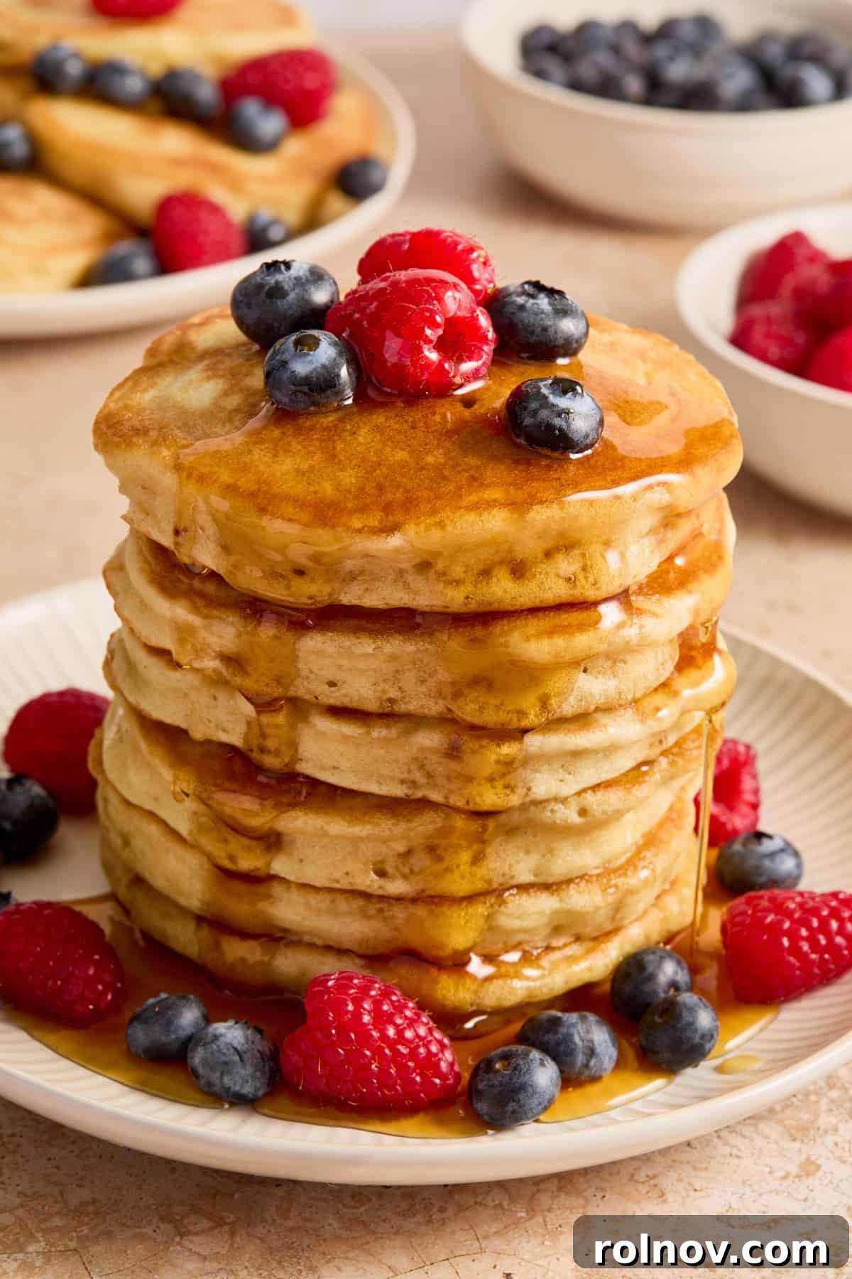 A stacked plate of golden dairy-free buttermilk pancakes, glistening with maple syrup and adorned with fresh mixed berries.