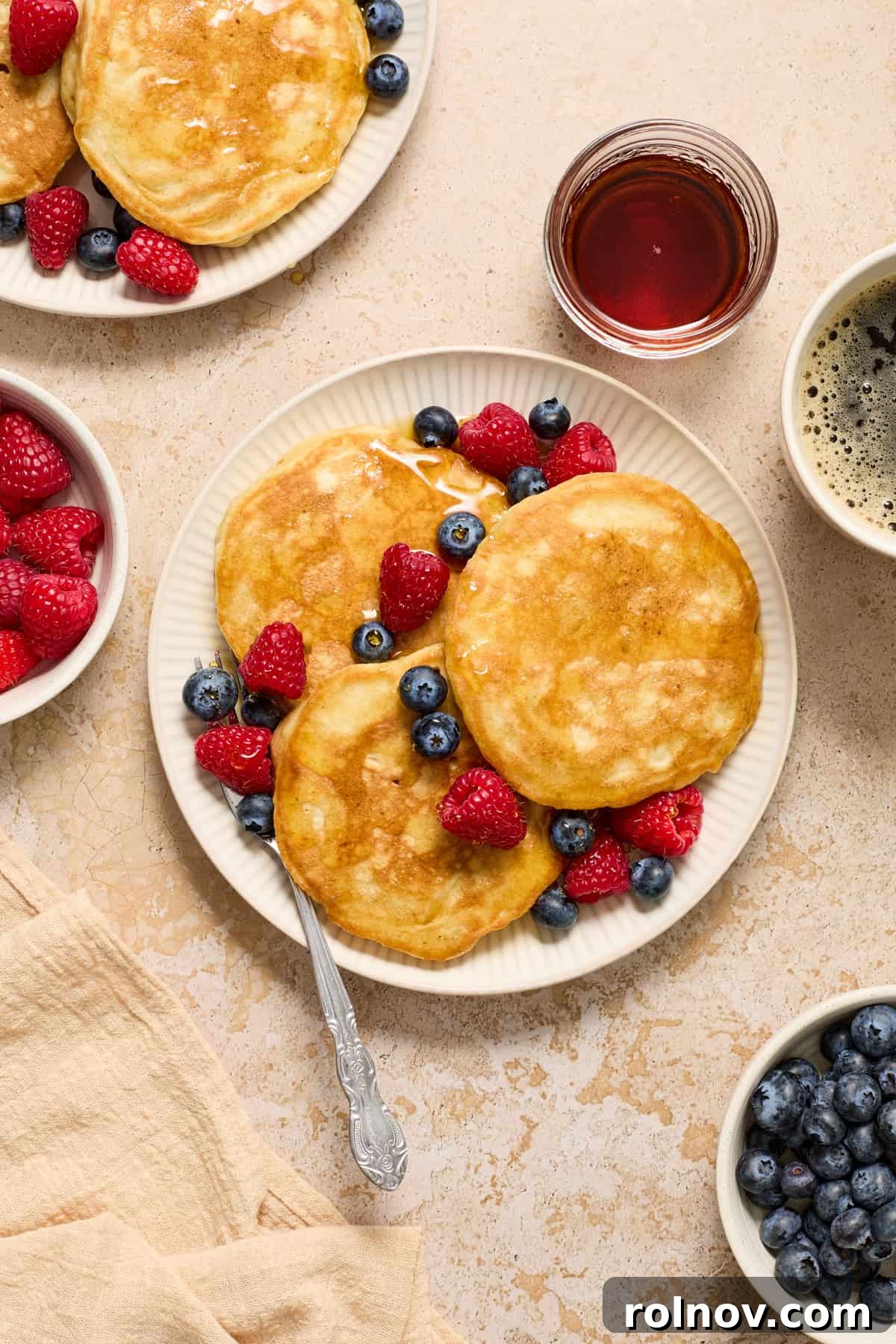 A beautiful close-up of dairy-free pancakes topped with vibrant blueberries and raspberries, with a fork resting beside them.