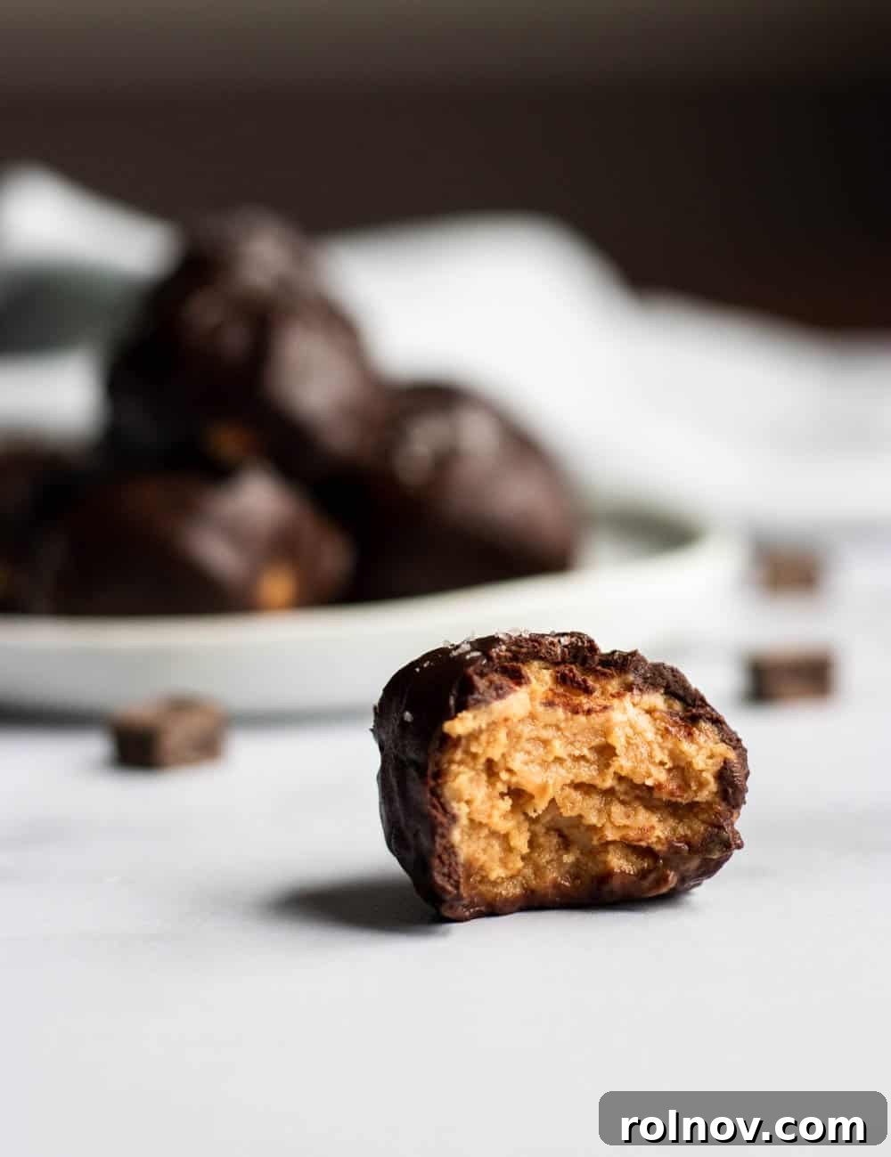 Decadent Homemade Peanut Butter Cup Truffles 2 Close-up of a homemade peanut butter cup truffle, showing a perfectly formed ball of peanut butter filling coated in smooth dark chocolate, resting on parchment paper.