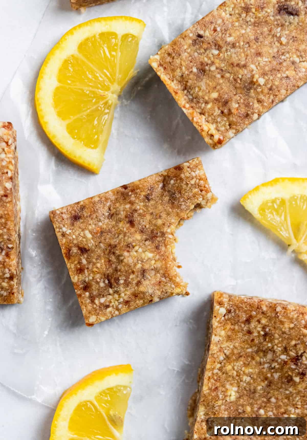 Tropical No-Bake Lemon Coconut Delights 2 Homemade Lemon Coconut Energy Bars on parchment with fresh lemon.