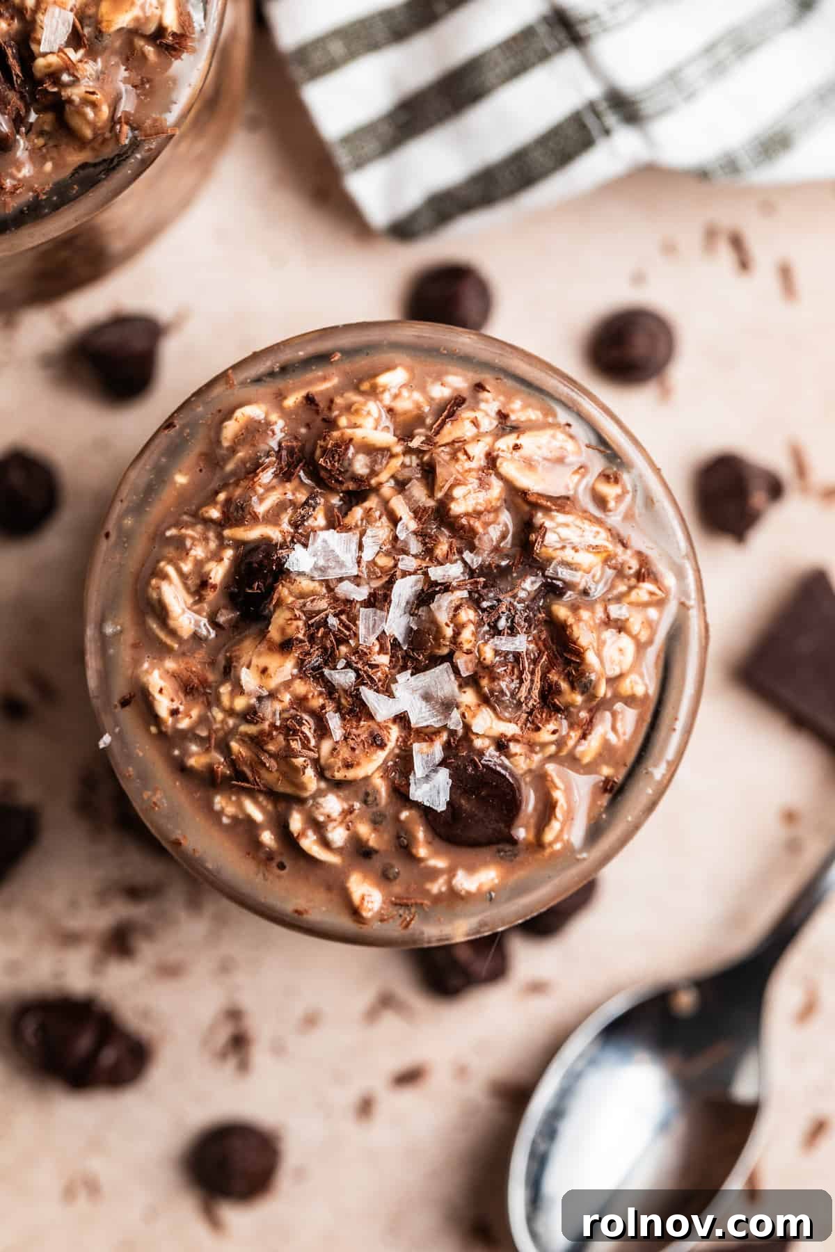 Overhead view of jar with chocolate oatmeal topped with coarse sea salt and spoon and chocolate chips surrounding.