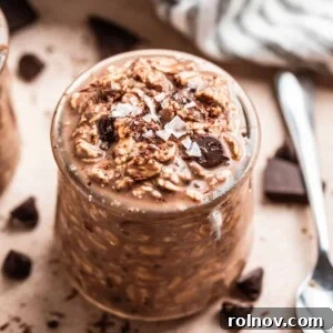Chocolate overnight oatmeal in jar with spoon and chocolate pieces beside it.