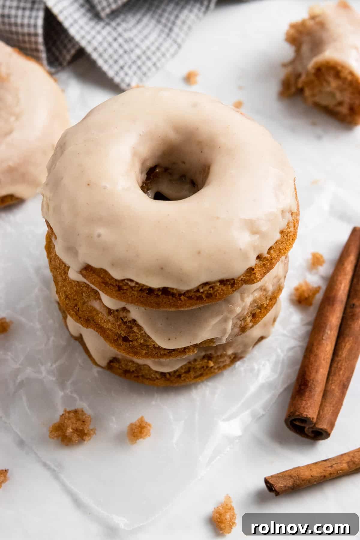 Stacked baked apple cinnamon donuts with a generous apple cider glaze, garnished with cinnamon sticks and fresh apple slices.
