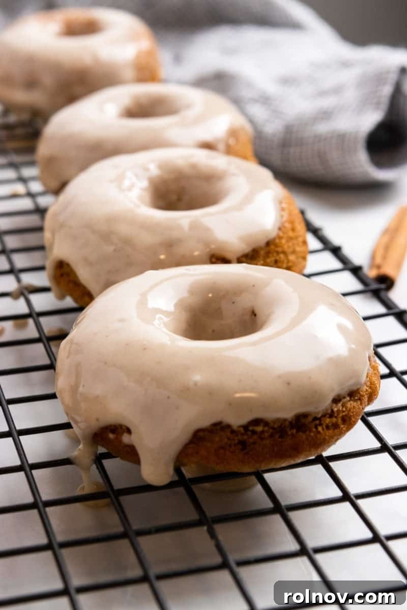 Freshly glazed baked donuts glistening on a wire cooling rack, ready to be served.