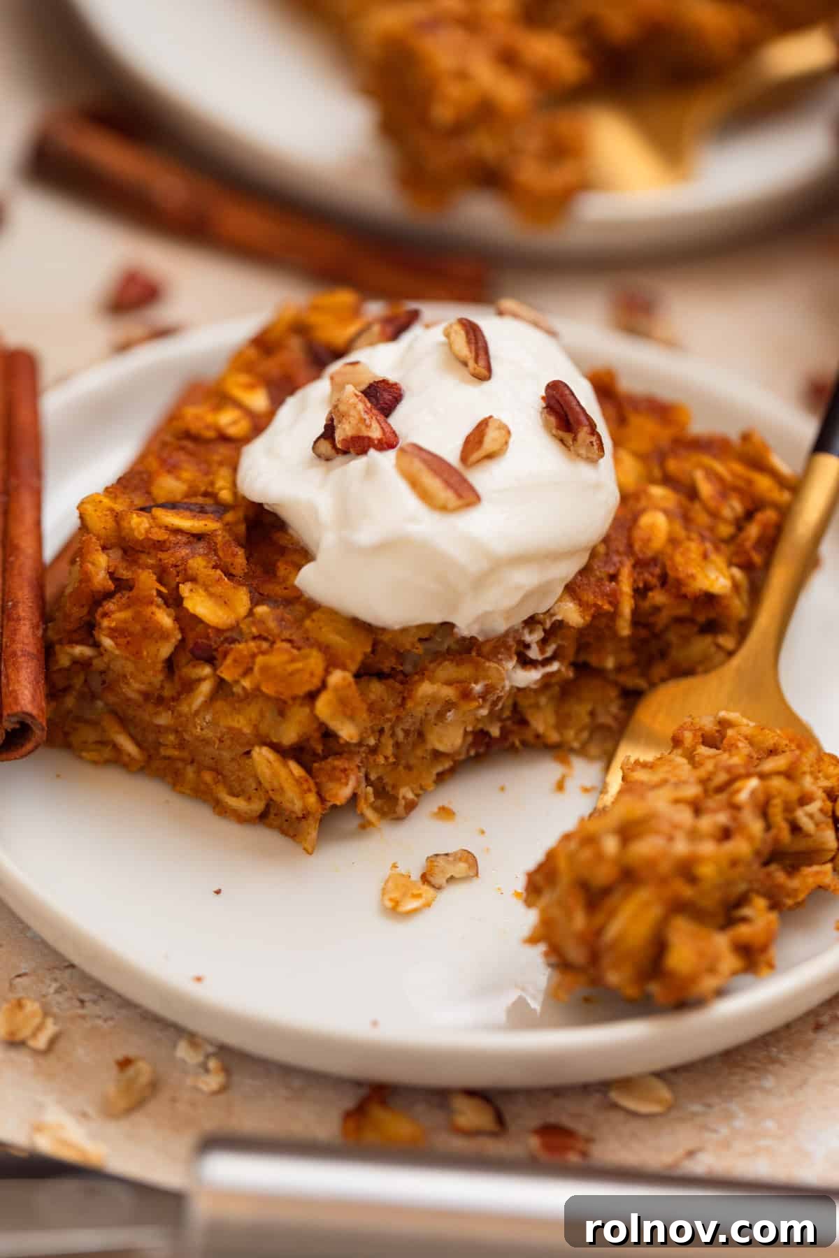 Spiced Pumpkin Oatmeal Bake 2 A delicious slice of pumpkin baked oatmeal on a white plate, garnished with creamy Greek yogurt and crunchy pecans, ready for a cozy fall breakfast.