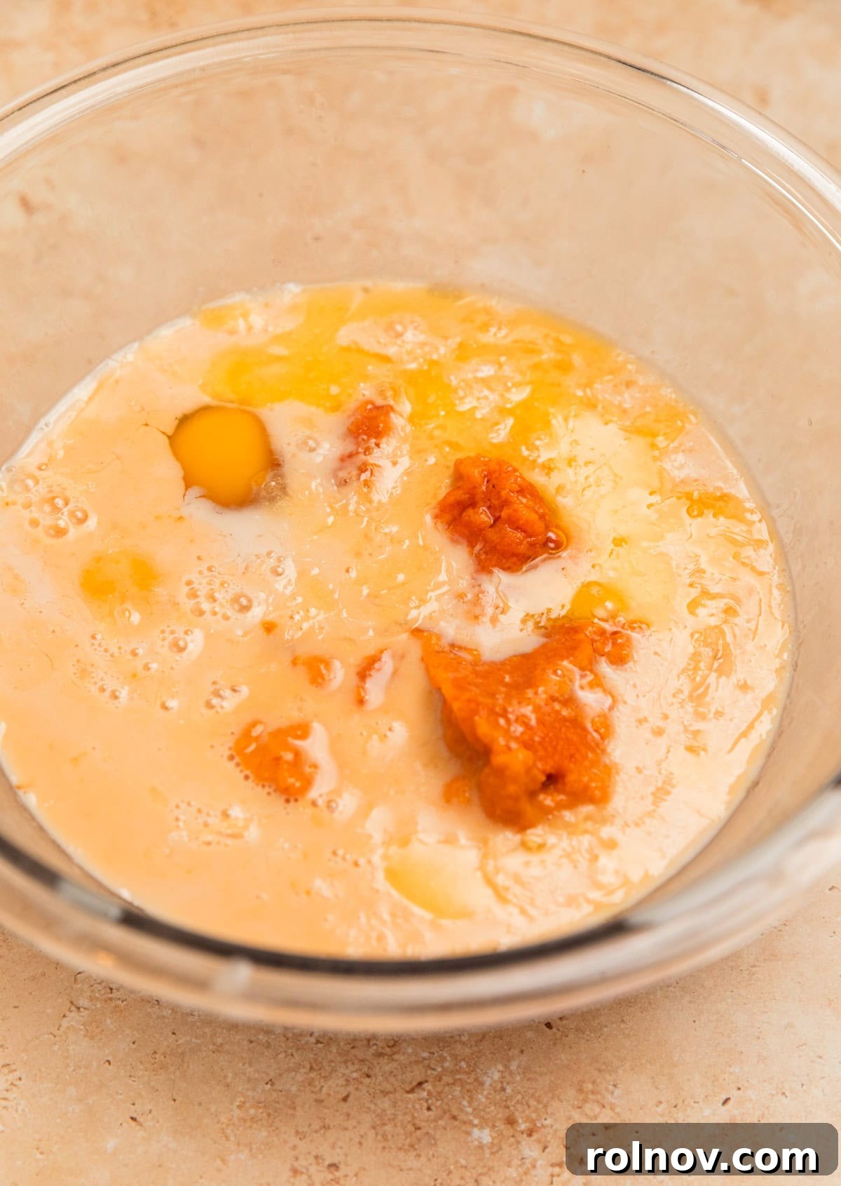 Spiced Pumpkin Oatmeal Bake 5 A glass mixing bowl holds the wet ingredients for pumpkin baked oatmeal, including milk, pumpkin purée, eggs, and maple syrup, ready to be whisked together.
