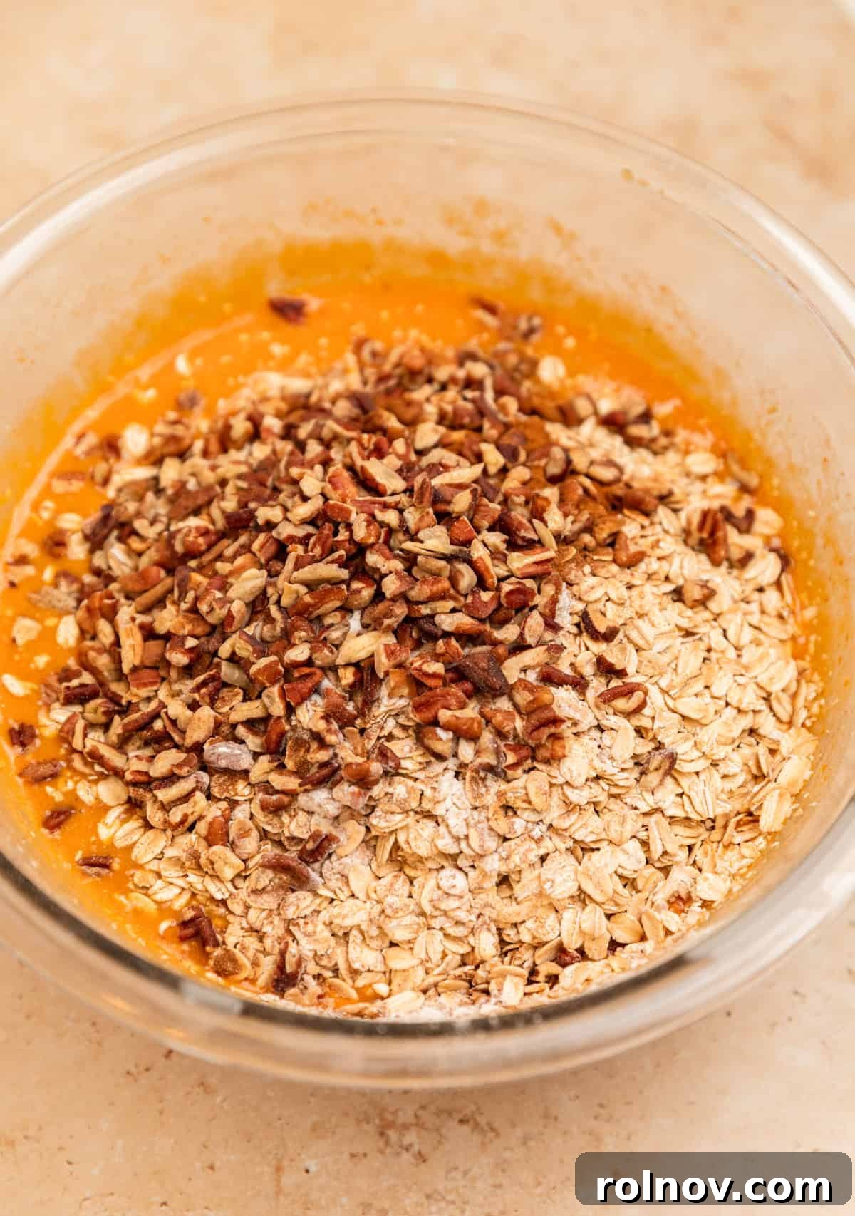 Spiced Pumpkin Oatmeal Bake 7 Rolled oats and chopped pecans are added to the whisked wet ingredients in a bowl, preparing for the final mix.
