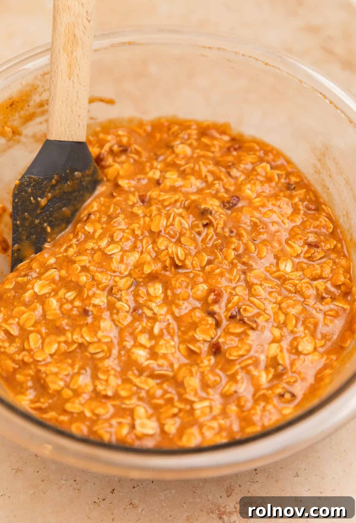 Spiced Pumpkin Oatmeal Bake 8 A spatula resting in a bowl containing the fully mixed pumpkin oatmeal batter, showcasing its thick and ready-to-bake consistency.