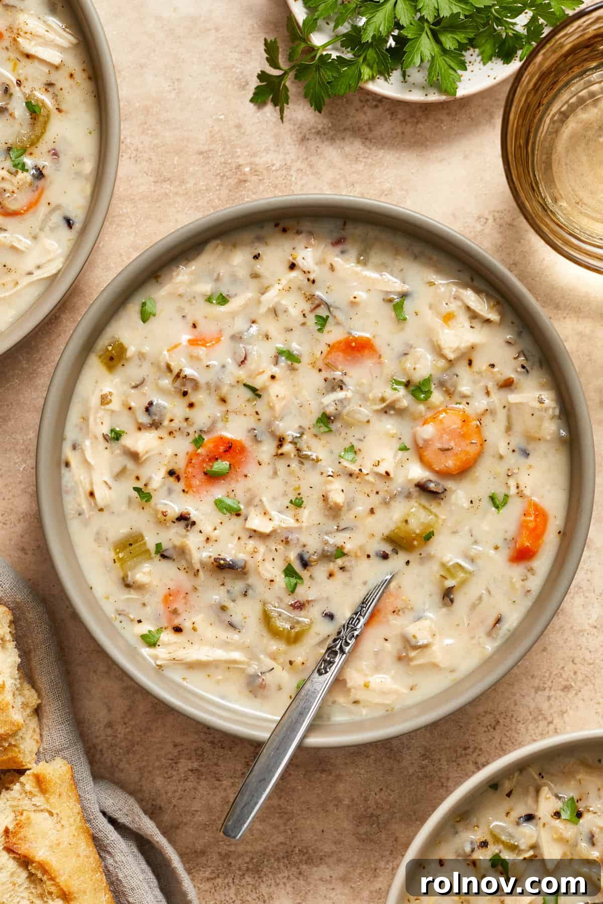 Crockpot chicken and wild rice soup in bowl with spoon scooping in, garnished with fresh herbs.