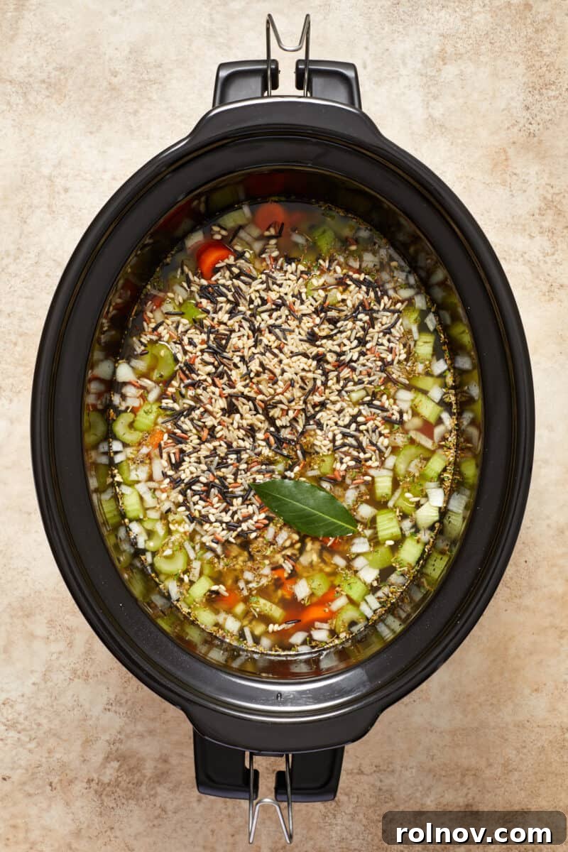Chicken and wild rice soup ingredients in slow cooker before cooked with bay leaf over top.