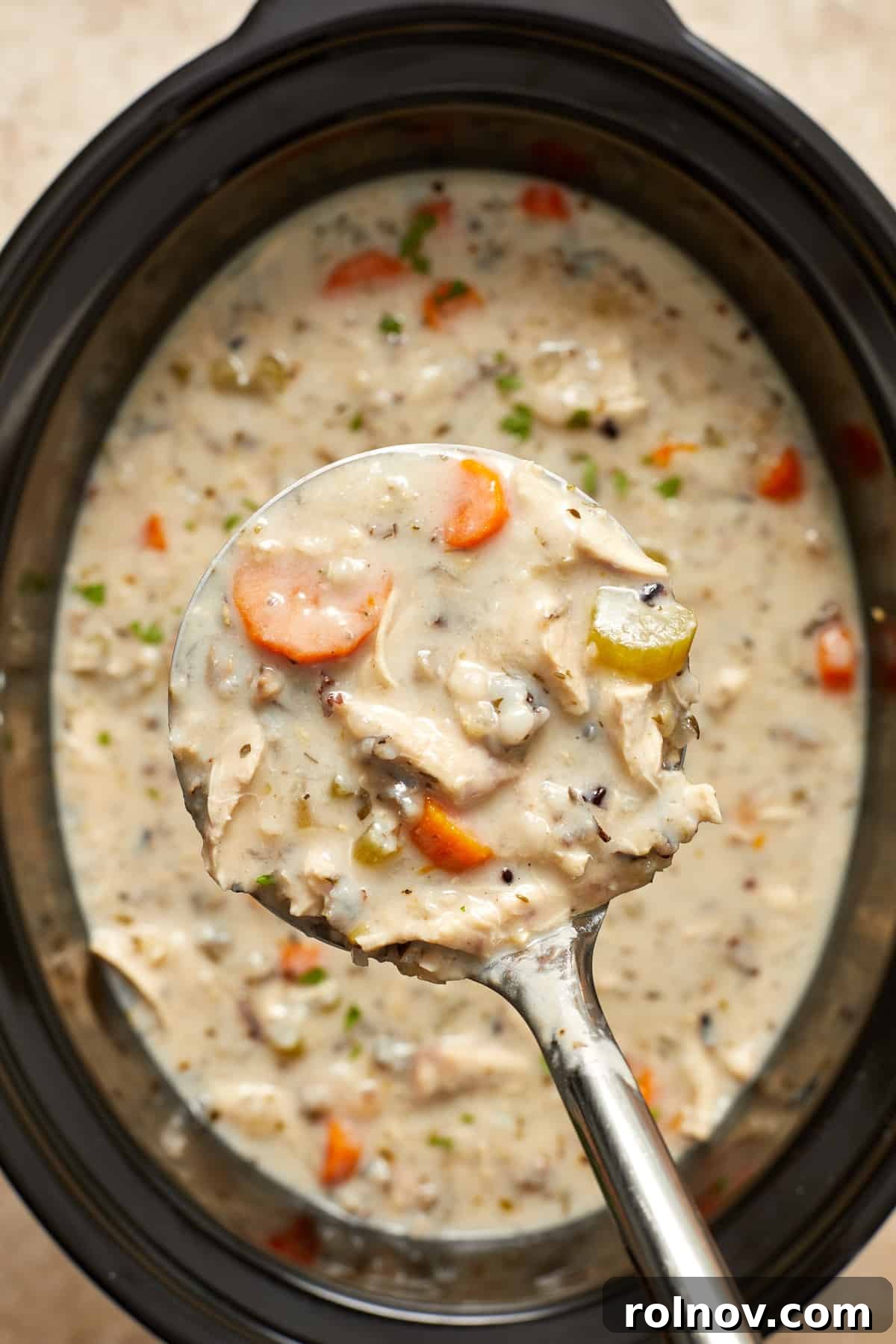 Close up view of crock pot chicken wild rice soup in ladle, showing creamy texture and visible ingredients.