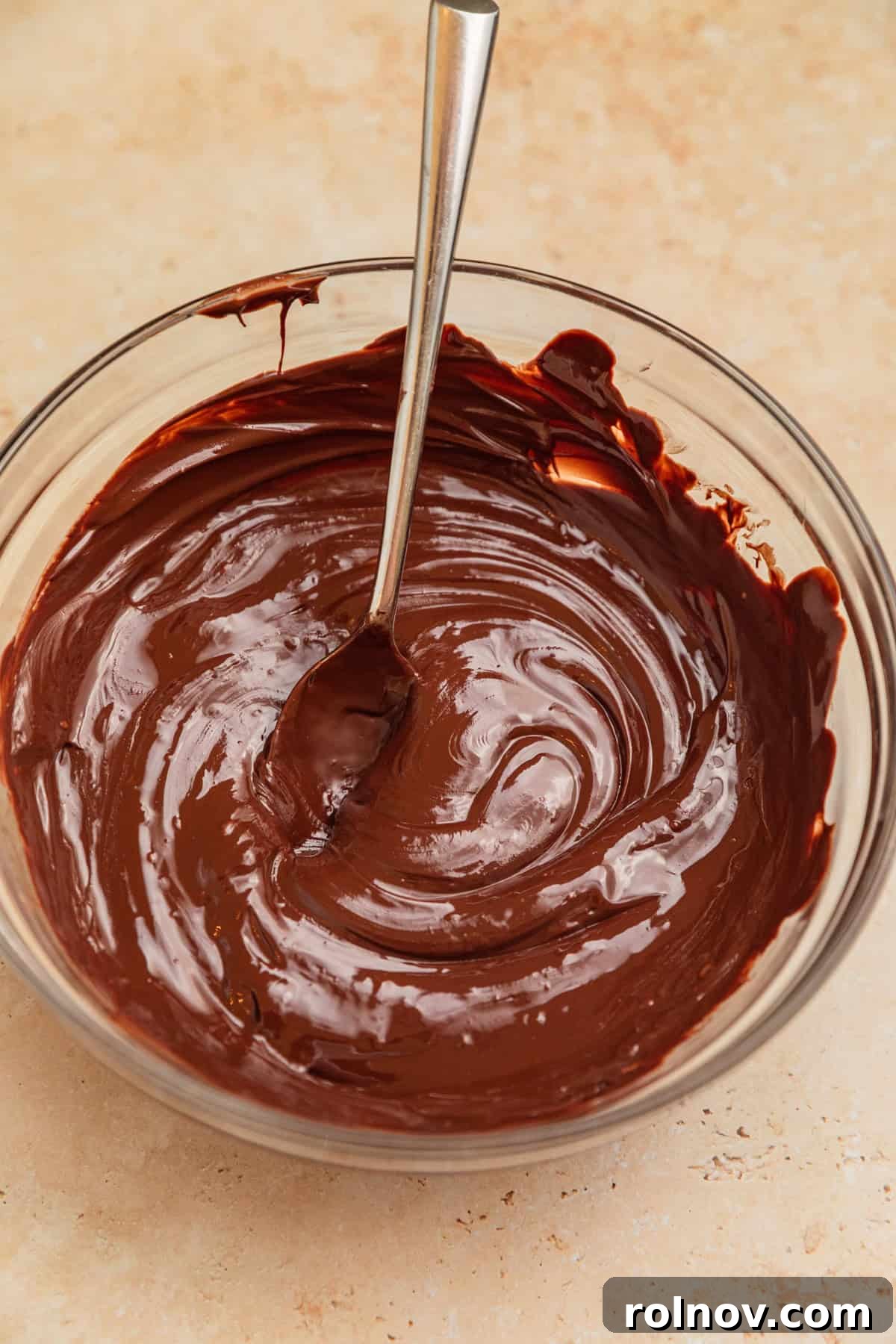 Reindeer Chow Delight 4 Melted dark chocolate in a microwave-safe bowl with a spoon, ready to be mixed.