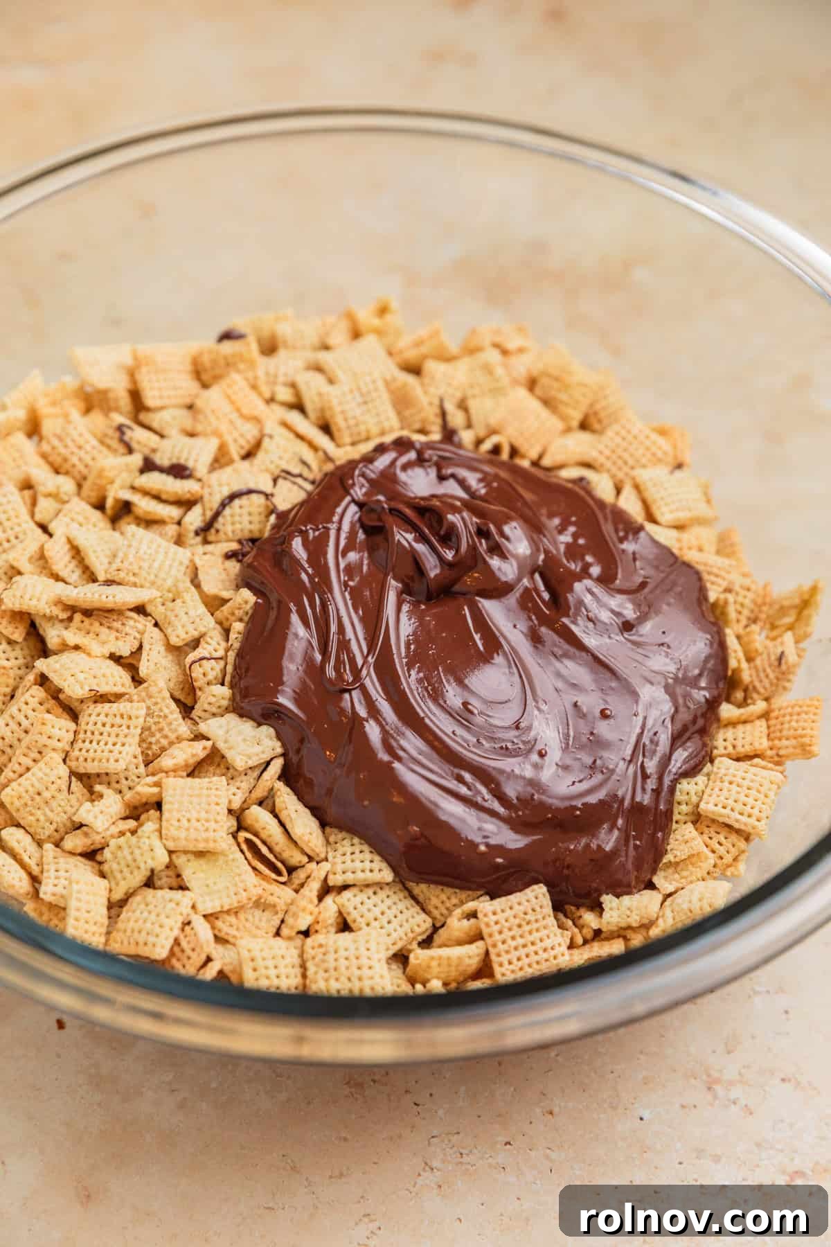 Reindeer Chow Delight 5 Melted dark chocolate mixture being poured over Rice Chex cereal in a large glass bowl.