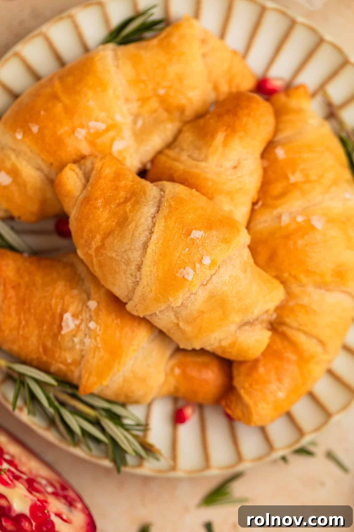 Golden Flaky Brie Bites 2 Pomegranate, brie and rosemary stuffed crescent rolls on plate, garnished with fresh rosemary.
