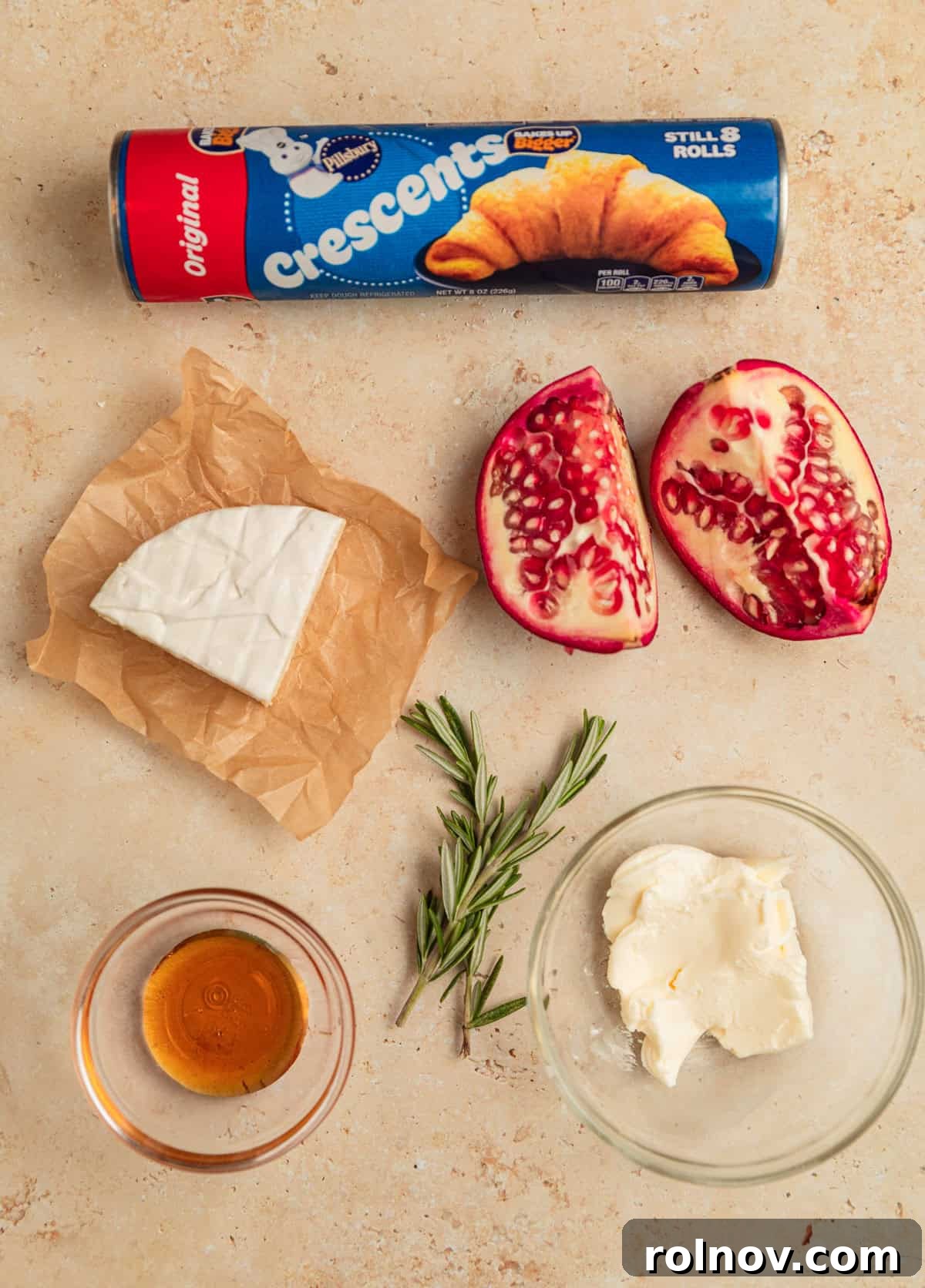 Golden Flaky Brie Bites 4 Crescent roll package, wedge of brie, rosemary sprigs and pomegranate arils laid out on a wooden surface.