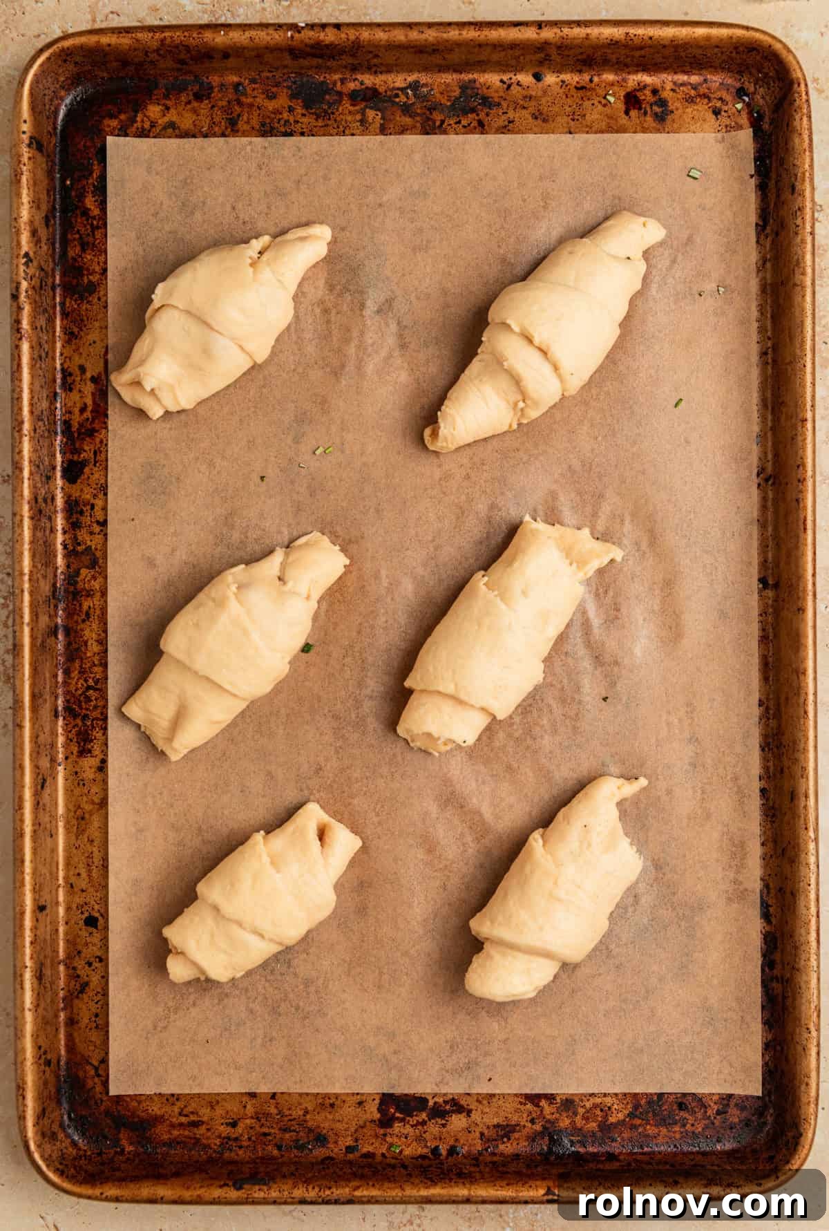 Golden Flaky Brie Bites 6 Crescent rolls tightly rolled and lined on a parchment-lined baking sheet, ready for baking.
