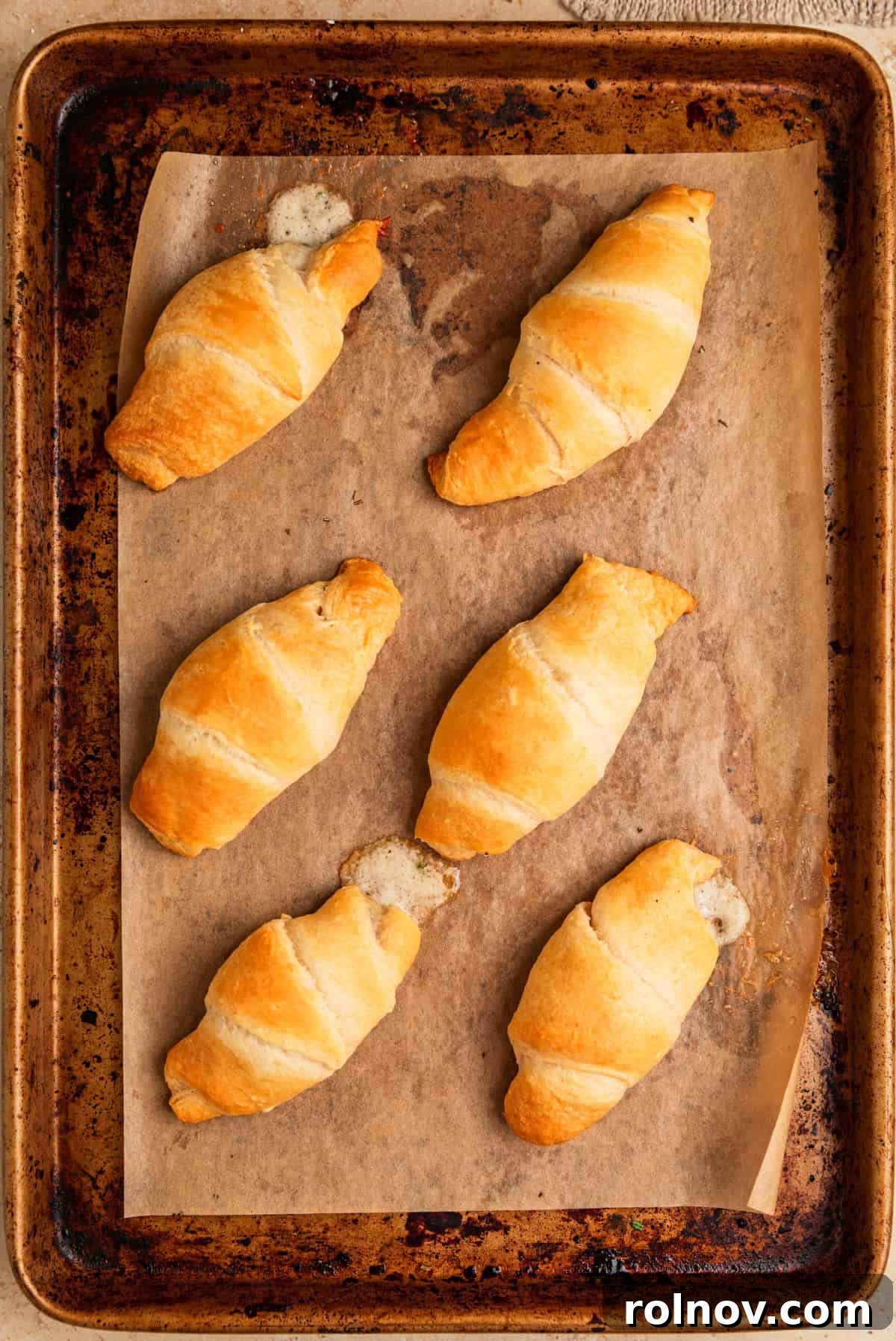 Golden Flaky Brie Bites 7 Freshly baked stuffed crescent rolls, golden brown, on a parchment-lined baking sheet.