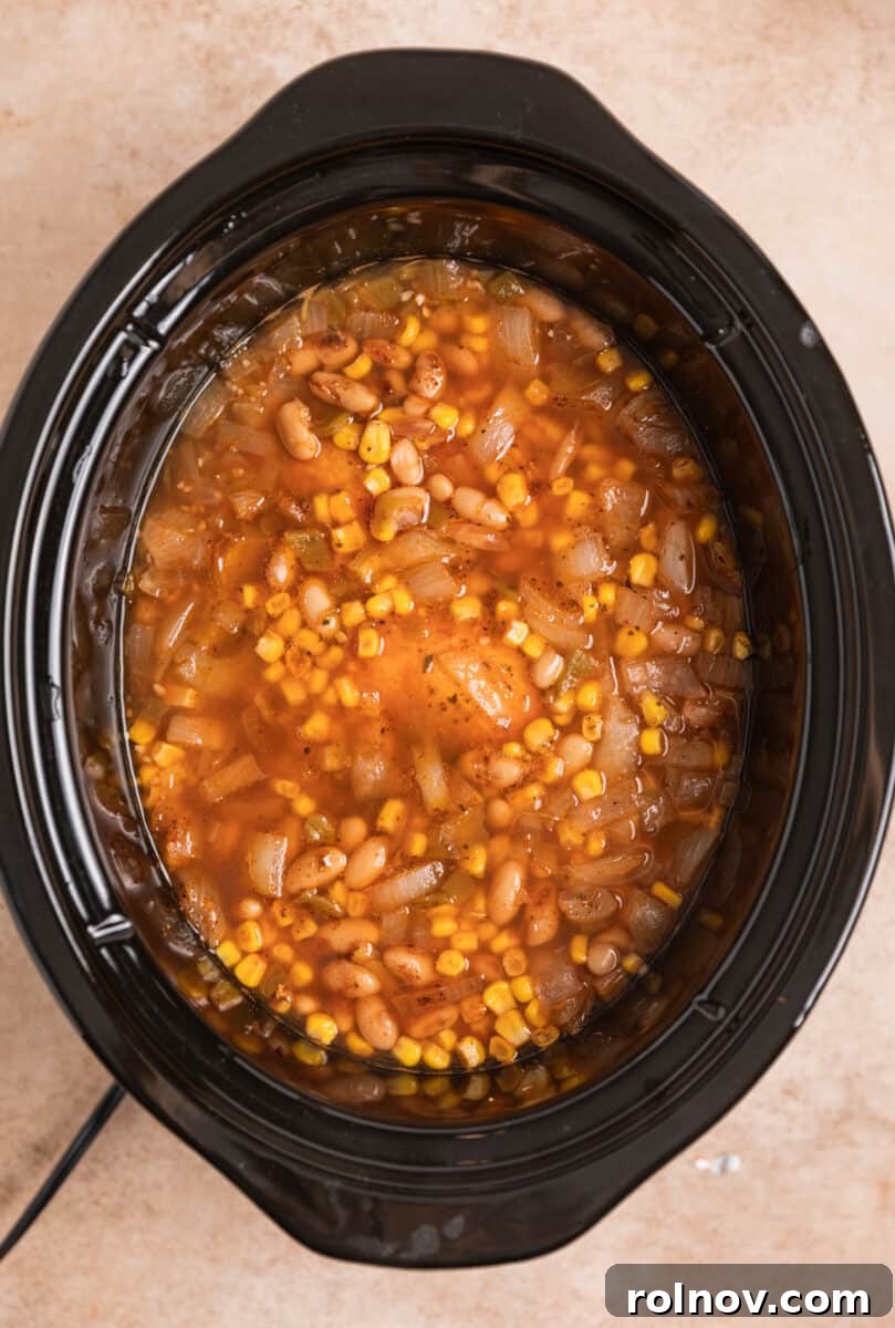 Cooked white chicken chili in the slow cooker, simmering before the chicken is removed for shredding.