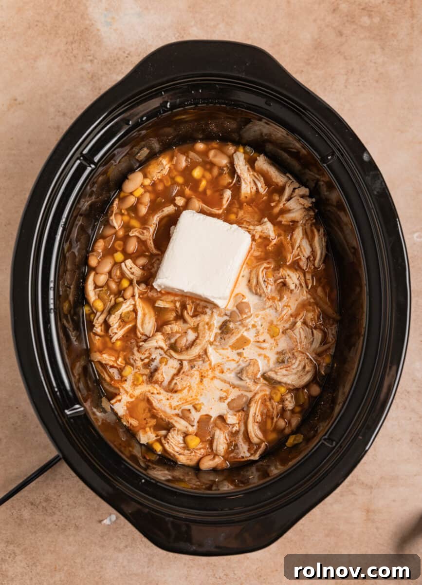 A block of cream cheese softening and melting into the hot white chicken chili in the slow cooker.