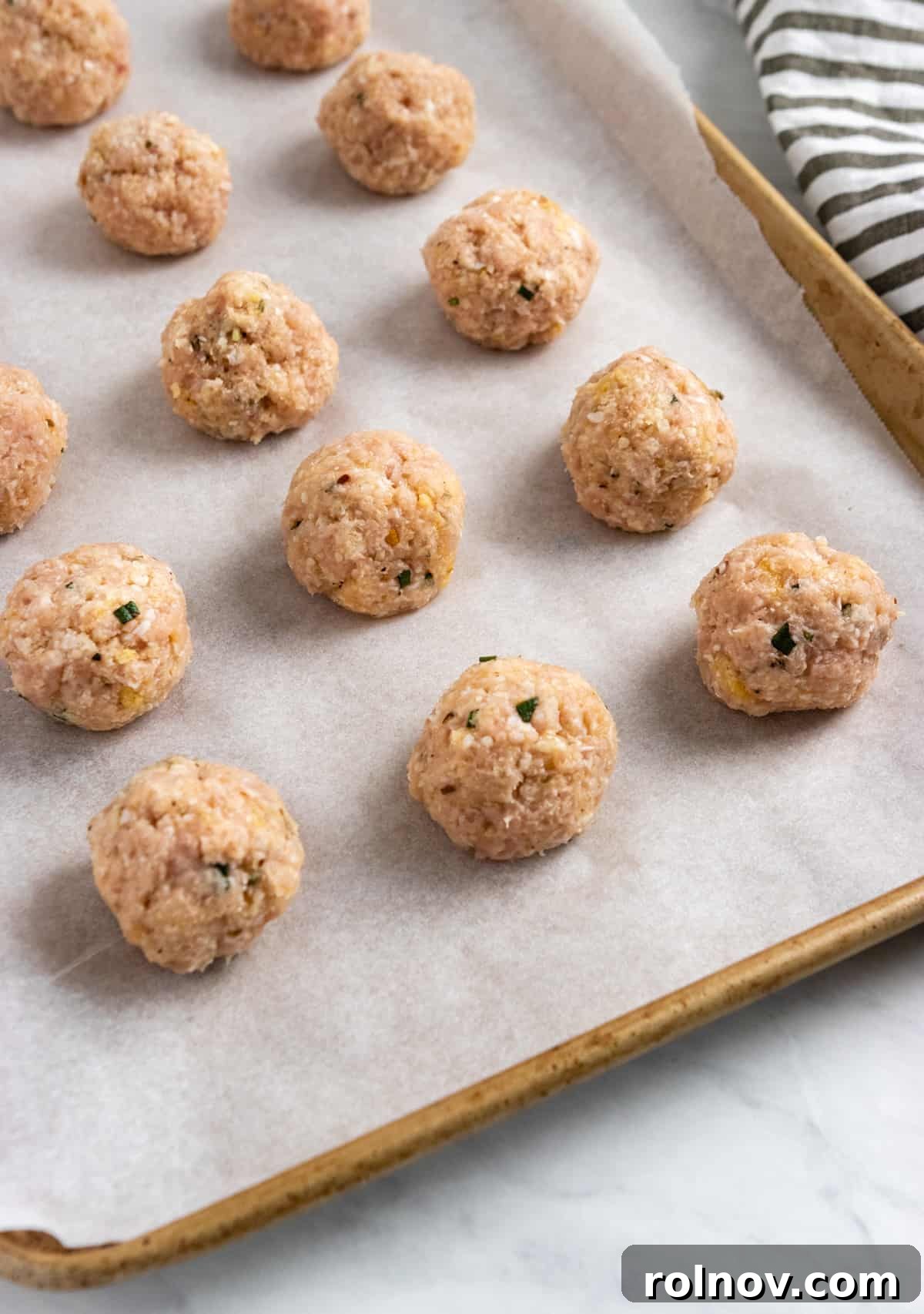 Oven-Baked Rosemary Parmesan Chicken Meatballs 4 Perfectly rolled chicken meatballs neatly arranged on a parchment-lined baking sheet, ready for the oven.