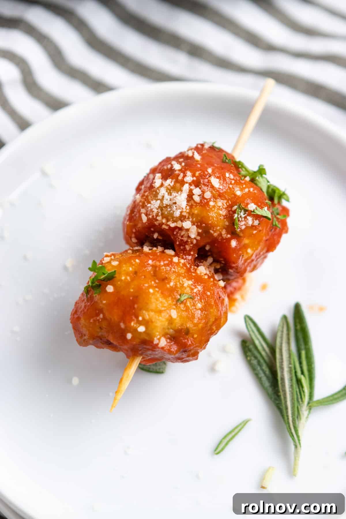 Oven-Baked Rosemary Parmesan Chicken Meatballs 5 Appetizer skewers featuring baked chicken meatballs generously coated in marinara sauce, garnished with fresh basil.