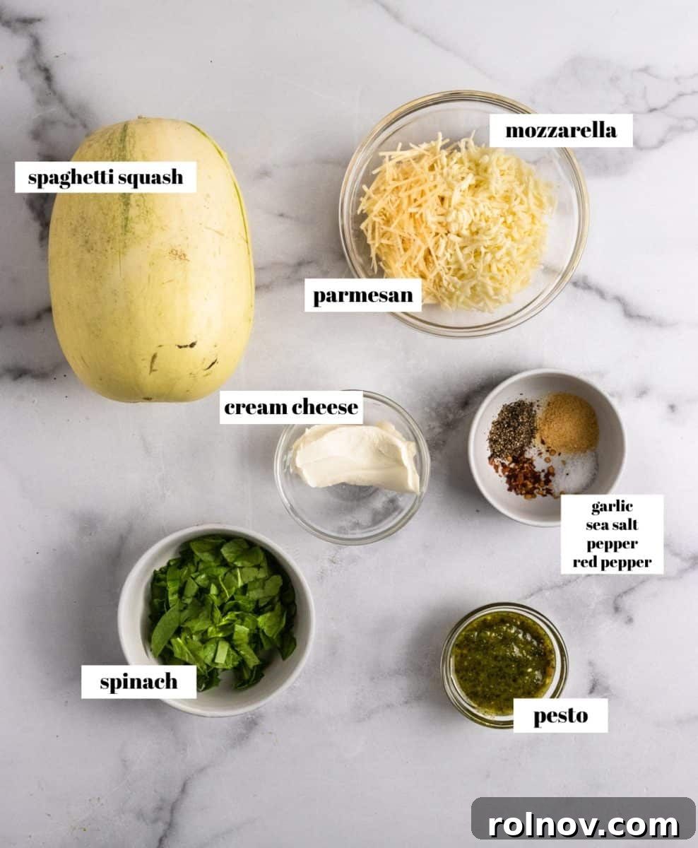 Luxe Pesto Spaghetti Squash Strands 3 Fresh ingredients laid out on a kitchen counter, including a cut spaghetti squash, spinach, cream cheese, pesto, and various cheeses, all ready for the recipe.