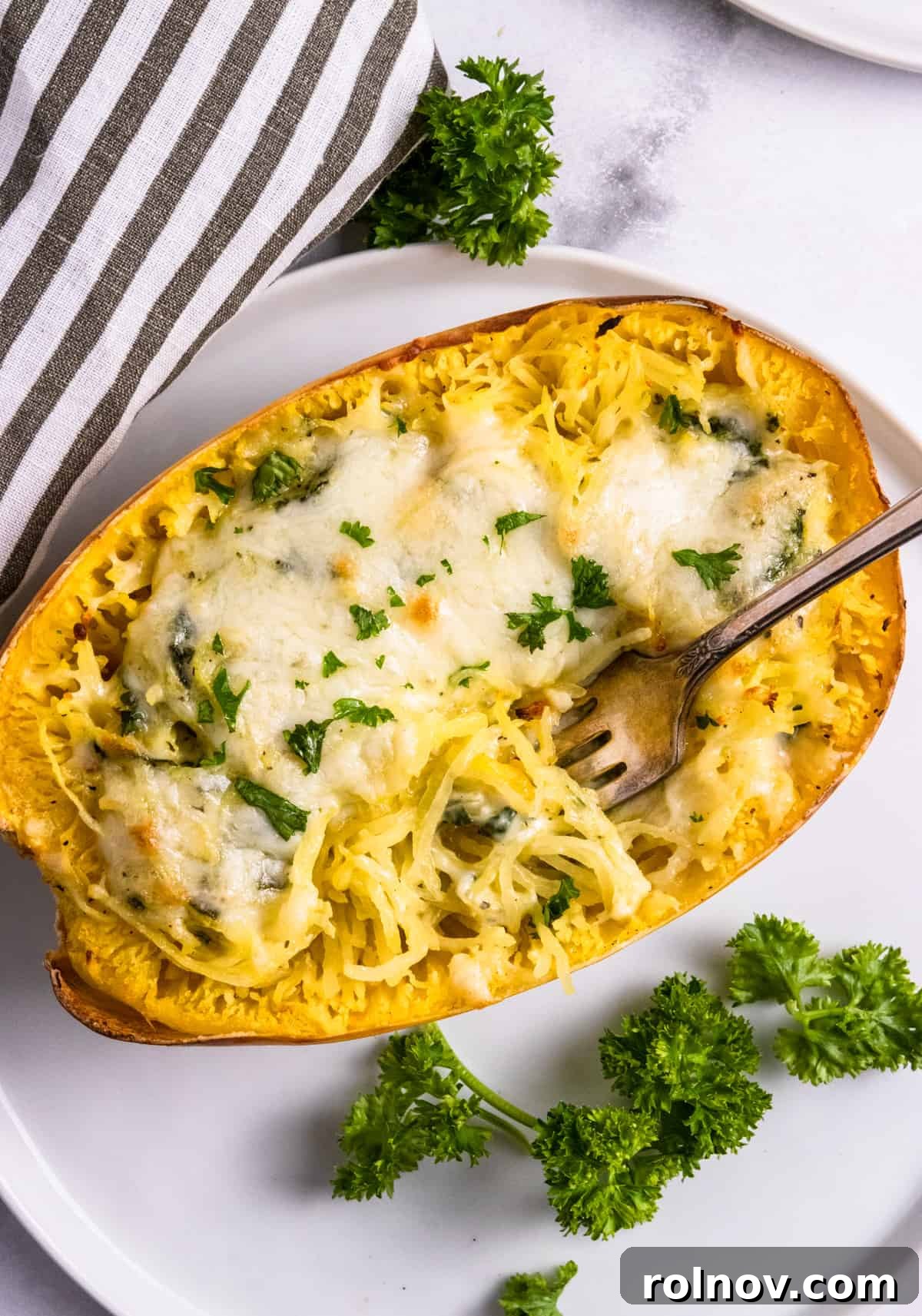 Luxe Pesto Spaghetti Squash Strands 7 A half of creamy pesto stuffed spaghetti squash, with a fork digging into the cheesy, flavorful strands.