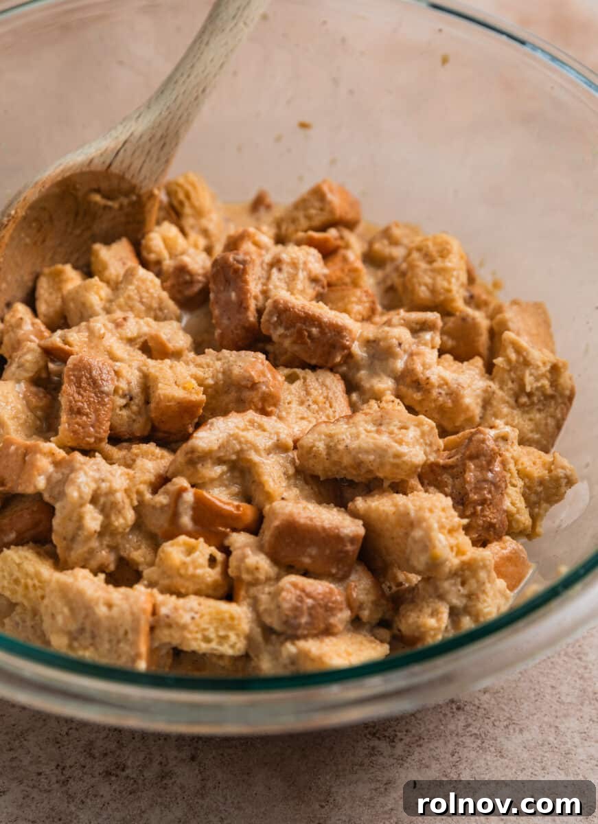 Golden French Toast Bites 7 Brioche bread pieces mixed with French toast egg mixture in bowl with wooden spoon.