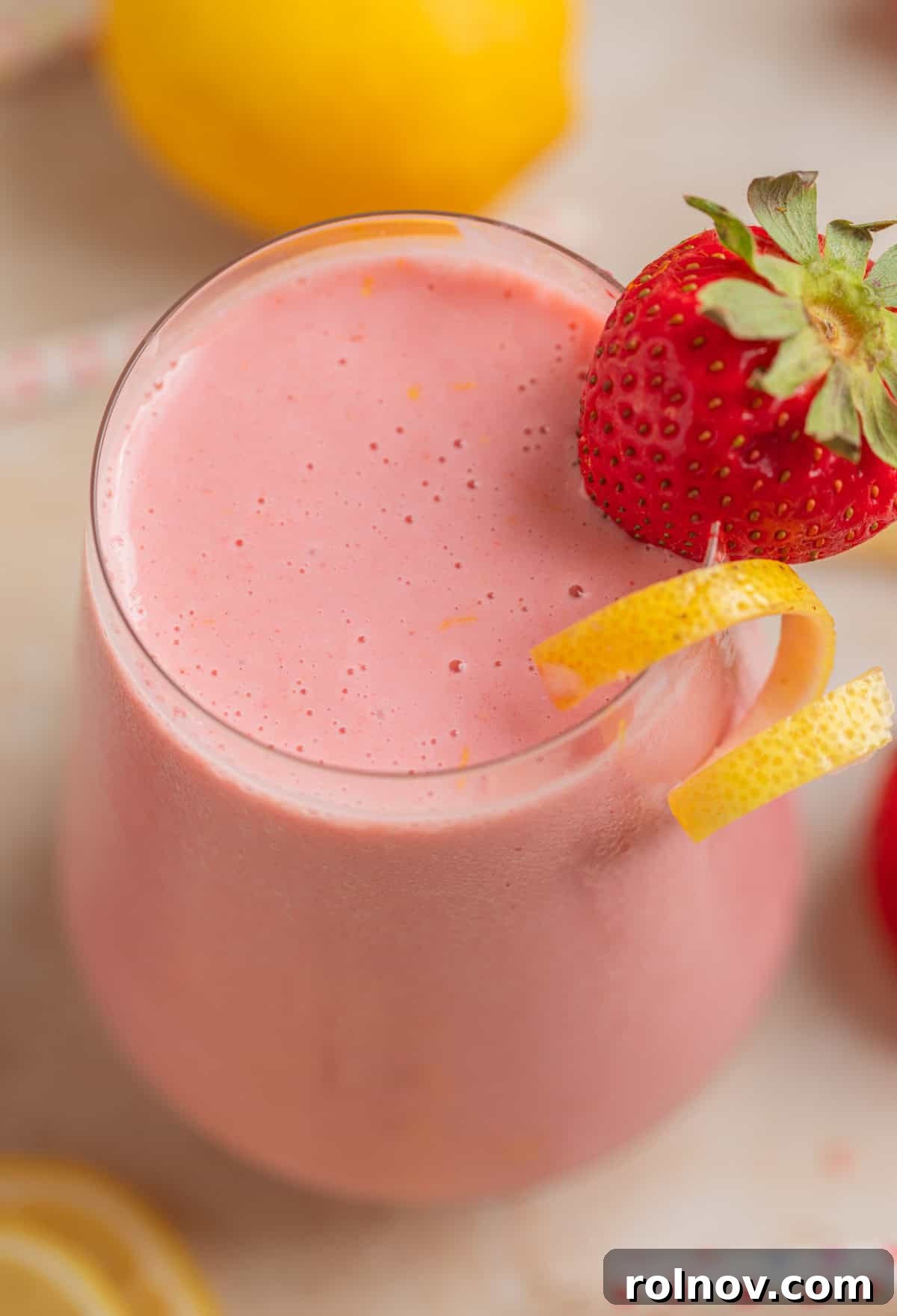 Pink Sunshine Smoothie 2 Strawberry lemonade smoothie in glass with lemon zest and strawberry garnish, sparkling with freshness.