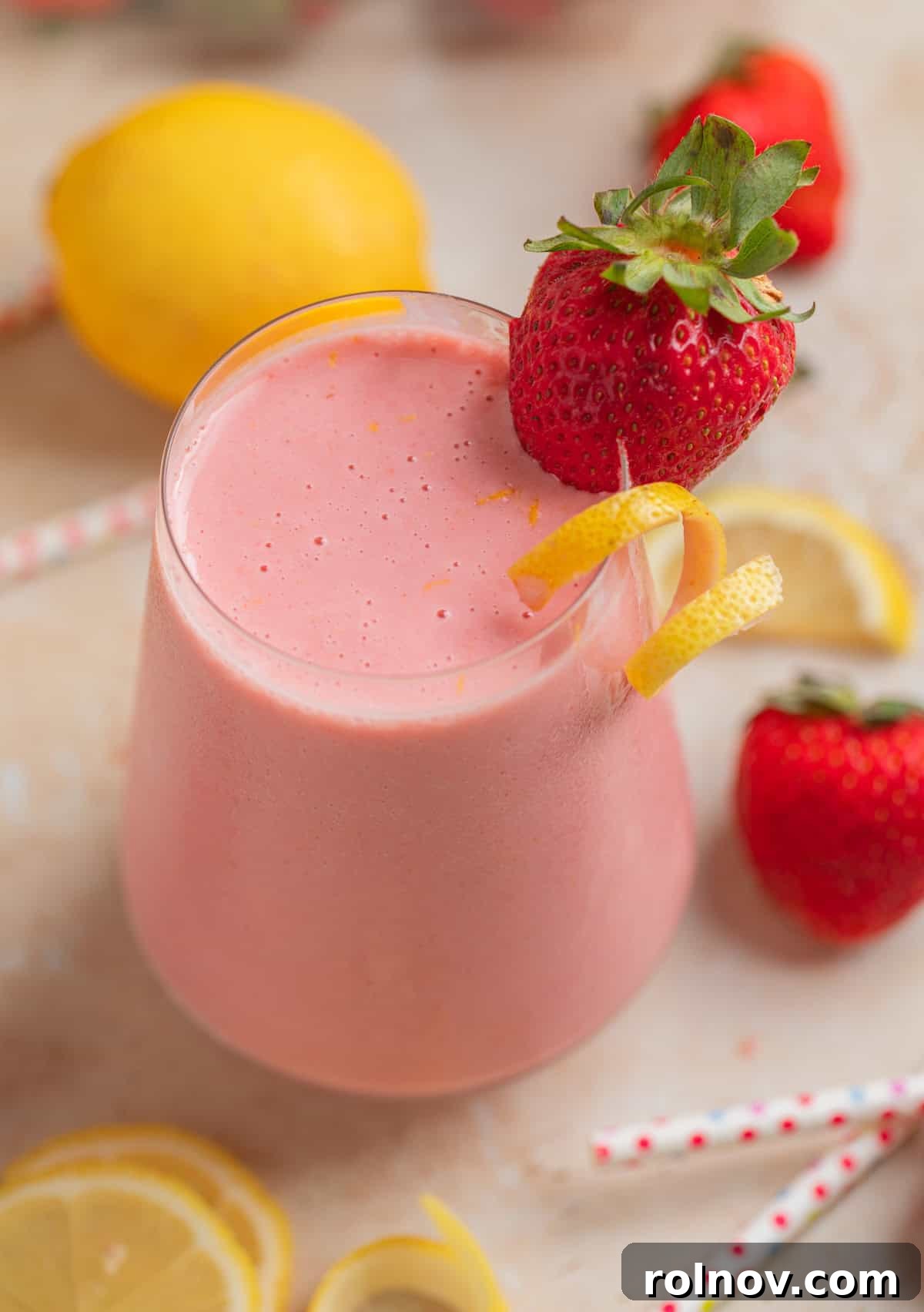 Pink Sunshine Smoothie 5 Smoothie in glass with lemon and strawberries and straws surrounding, ready to be enjoyed.