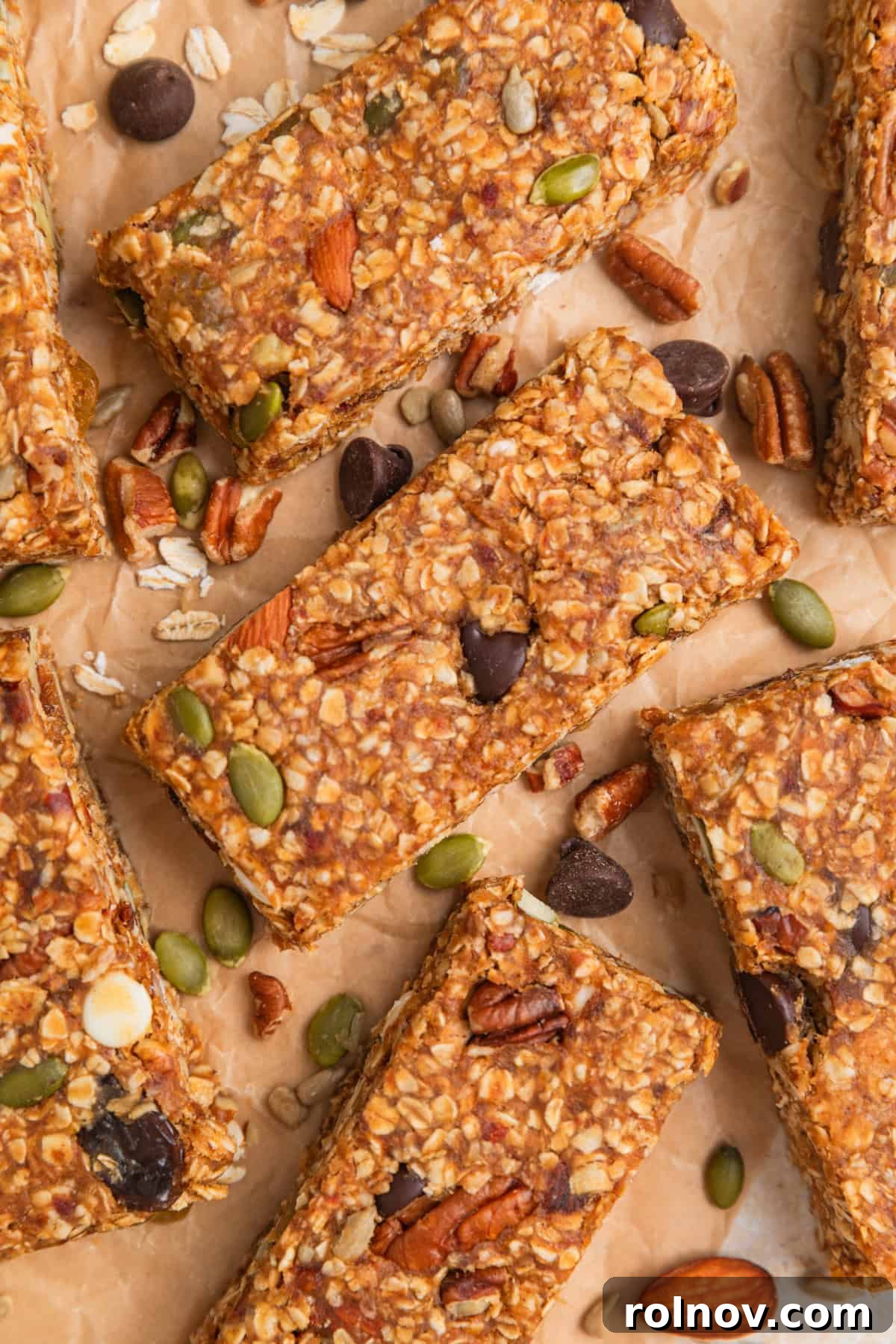 Adventure Fuel Bars 13 No bake trail mix oatmeal bars arranged on parchment paper, surrounded by loose almonds, oats, and chocolate chips, highlighting the ingredients.